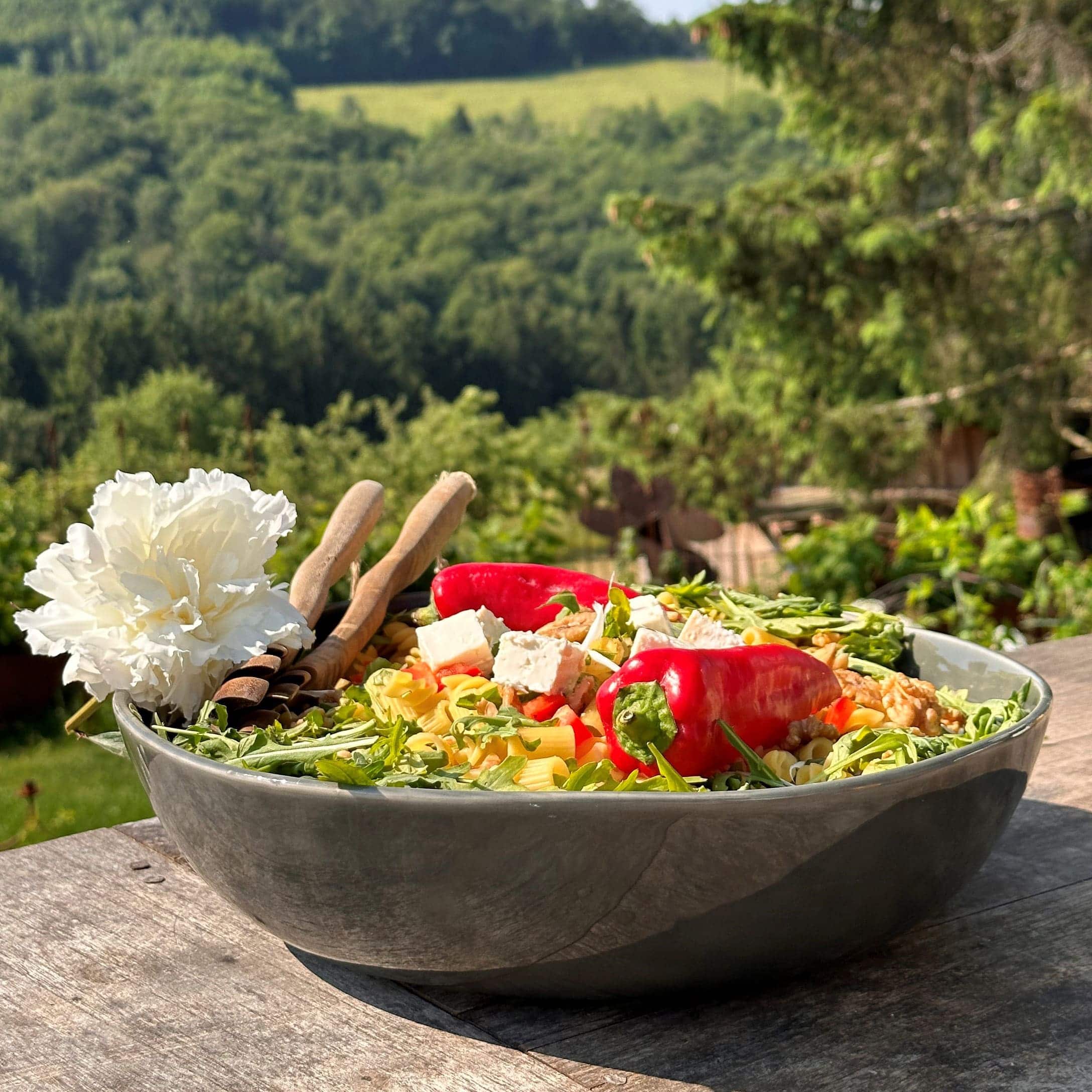 Große Keramikschüssel mit Salat, roter Paprika, Feta und Rucola auf Holztisch im Freien