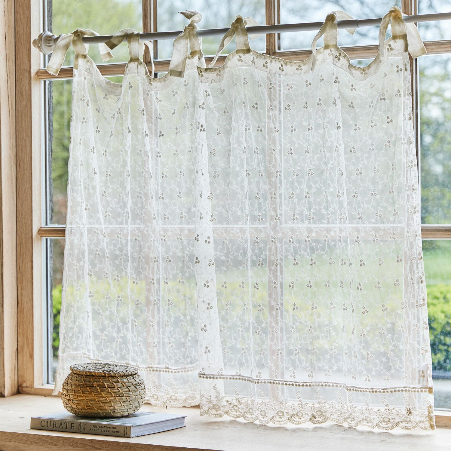 Scheibengardine Auradé Transparenter, bestickter cremefarbener Vorhang mit Schleifen an einem Fenster mit Gartenblick