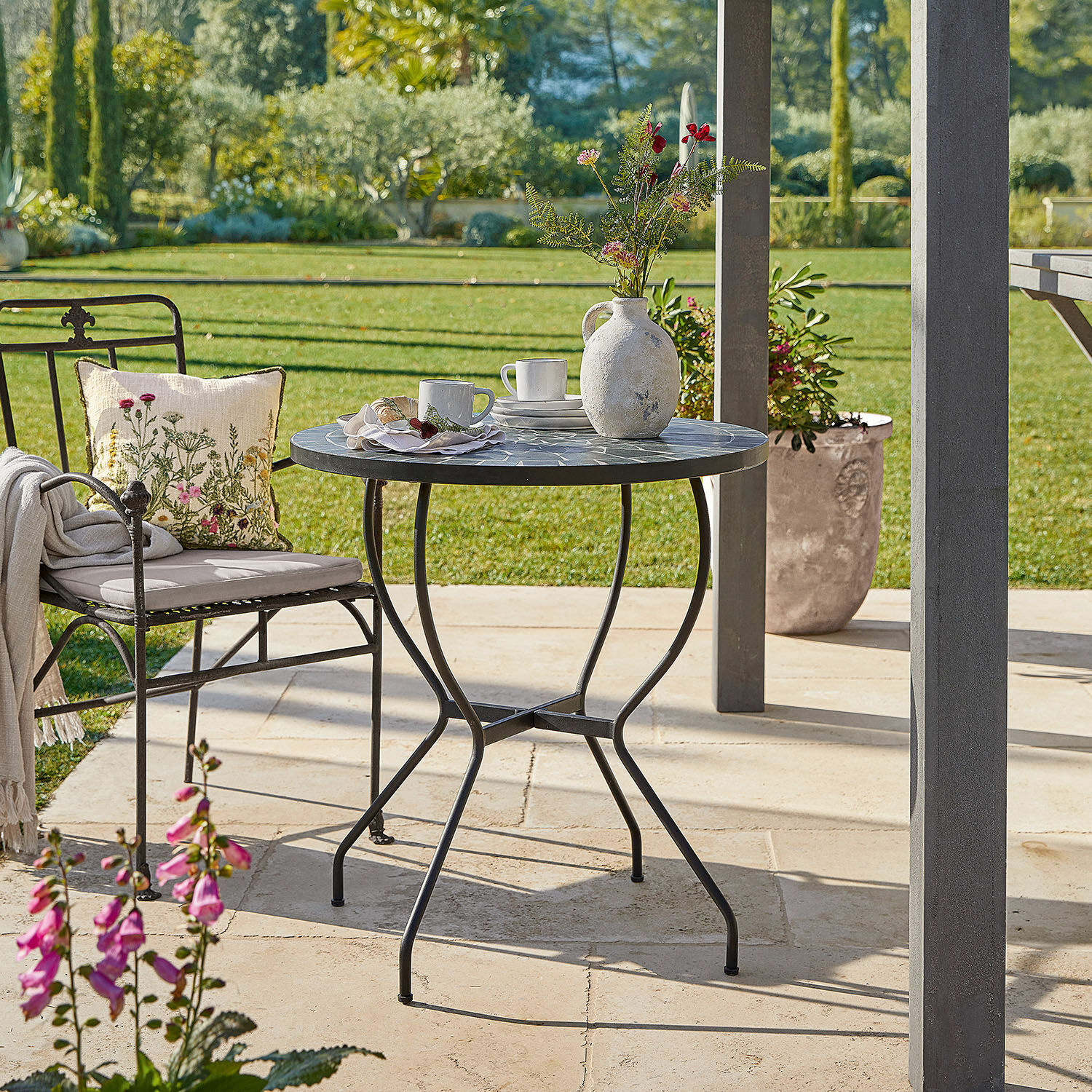 Tisch Ballaigues Runder Gartentisch mit Metallgestell und grauer Mosaikplatte auf sonniger Terrasse