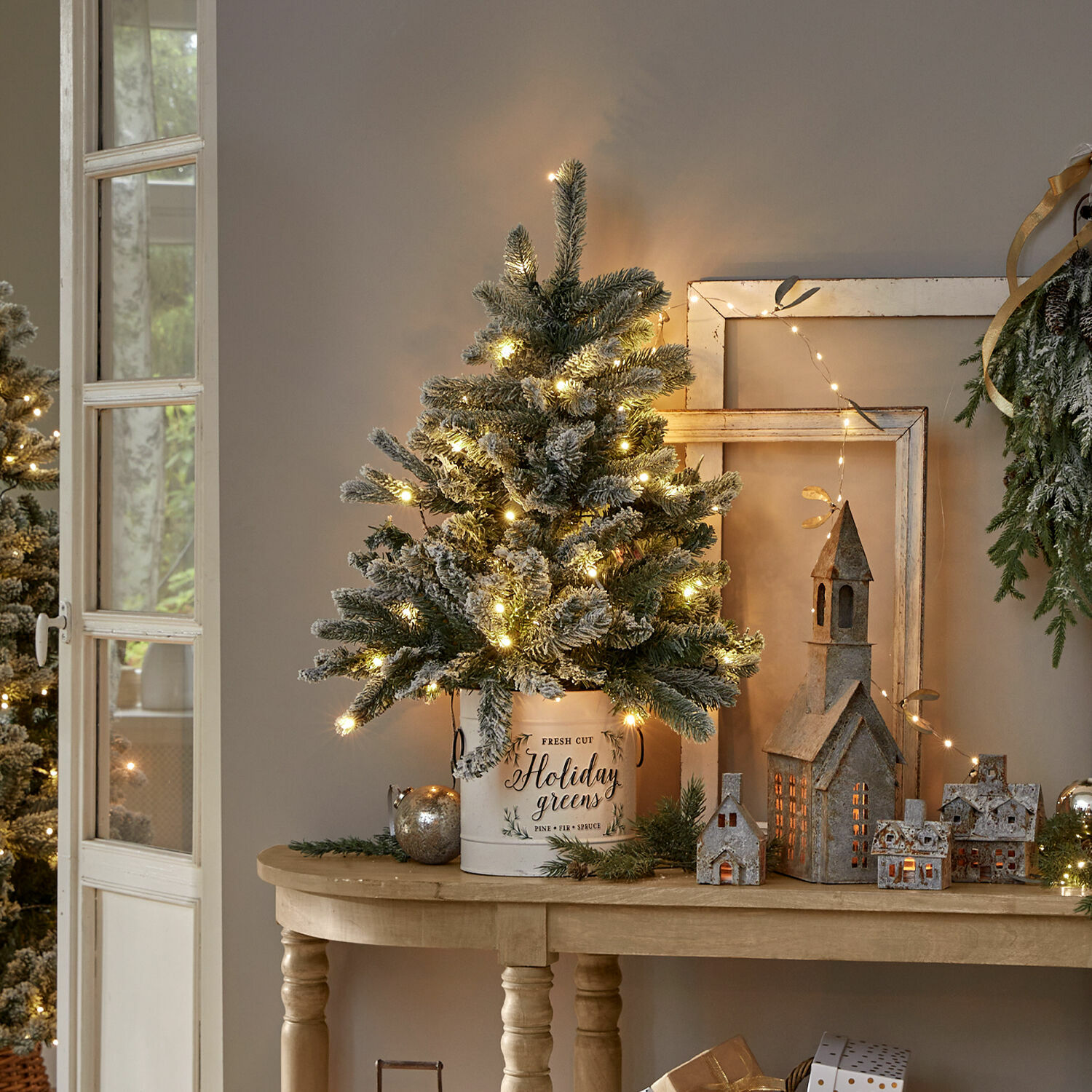 Weihnachtsbaum Mannier Weihnachtsdeko mit beleuchtetem künstlichen Tannenbaum in weißem Metallkübel auf Holztisch
