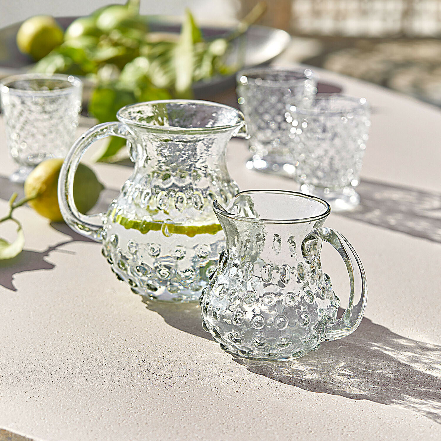 Glaskrug und kleines Glas mit erhabener Struktur auf hellem Tisch, ideal für Sommergetränke