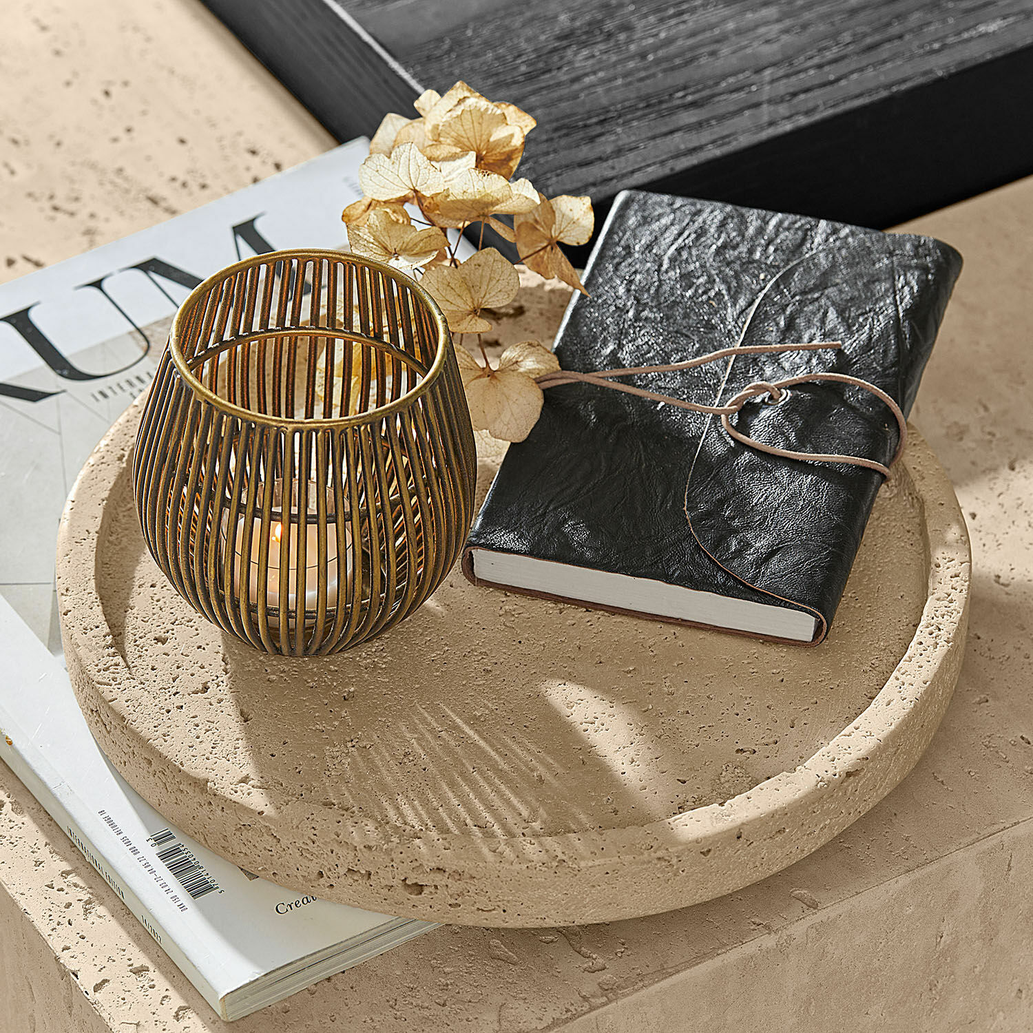 Runder beige Steintablett mit schwarzem Lederjournal und goldenem Metall-Teelichthalter