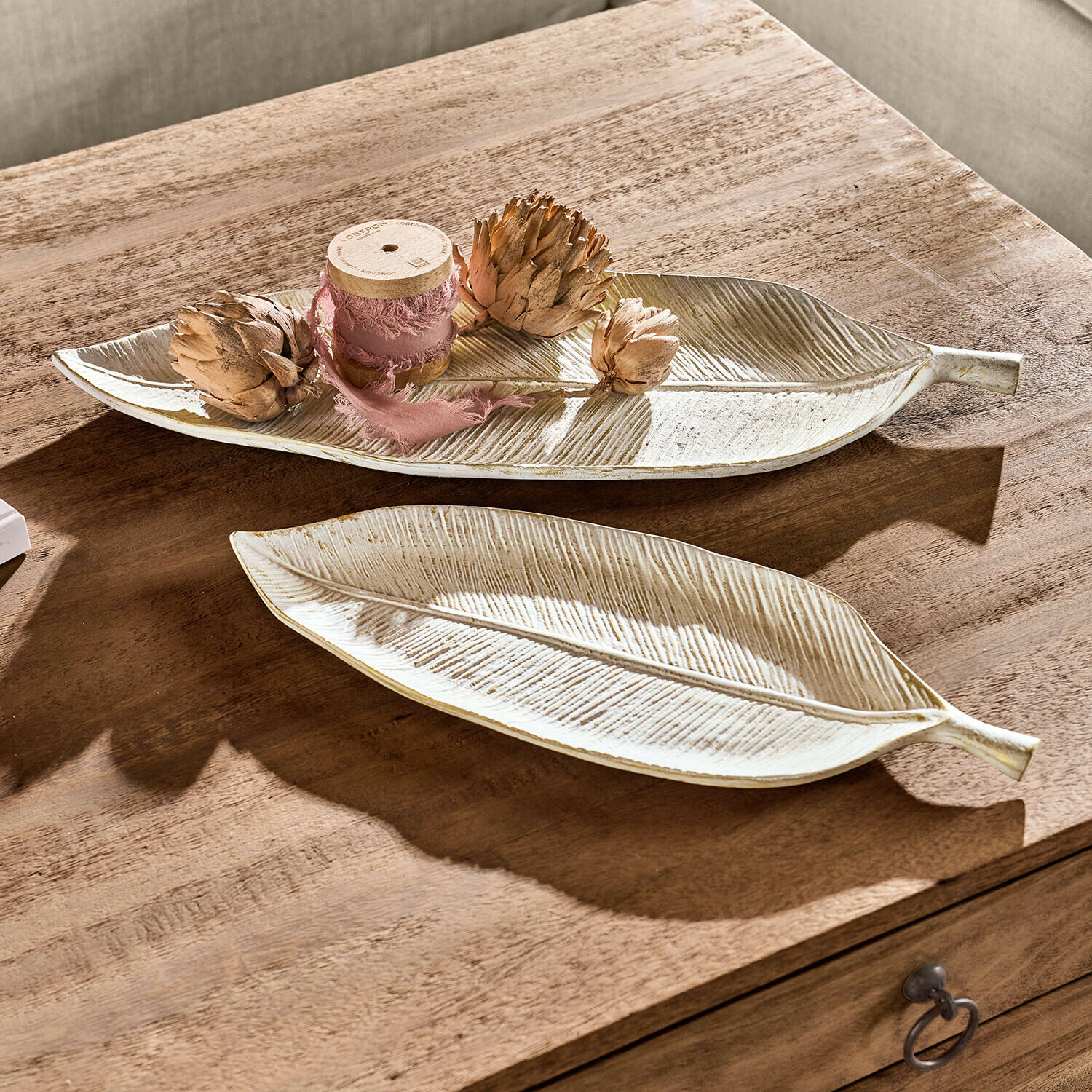 Dekorative Keramikteller in Blattform in Creme auf einem Holztisch arrangiert