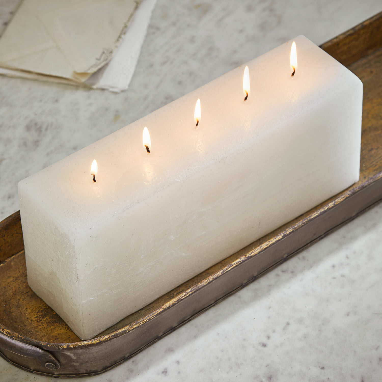 Weiße rechteckige Kerze mit fünf brennenden Dochten auf dekorativem Metalltablett