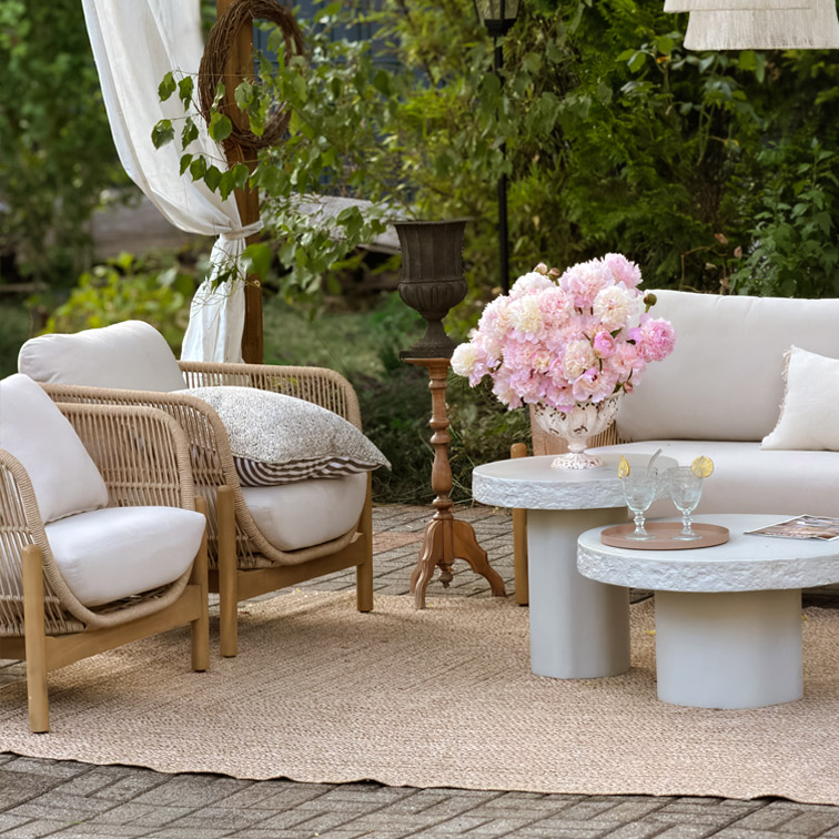 Gartenmöbel-Set mit hellen Kissen, Rattansesseln und Betontischen auf Juteteppich im Außenbereich