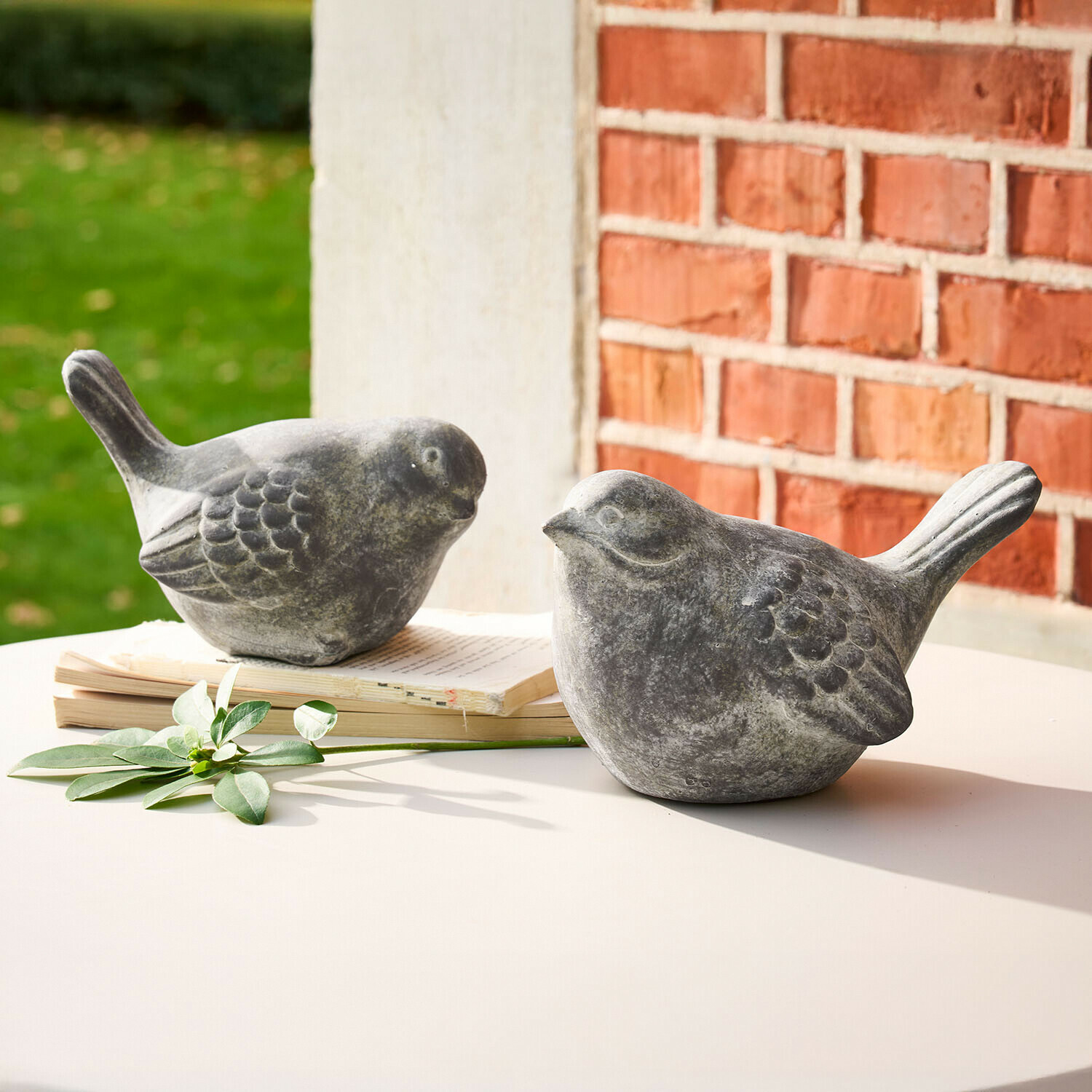 Deko-Vogel 2er Set Haldoríe Zwei graue Vogel-Figuren aus Stein auf weißem Tisch mit Buch und grünem Blatt als Dekoration
