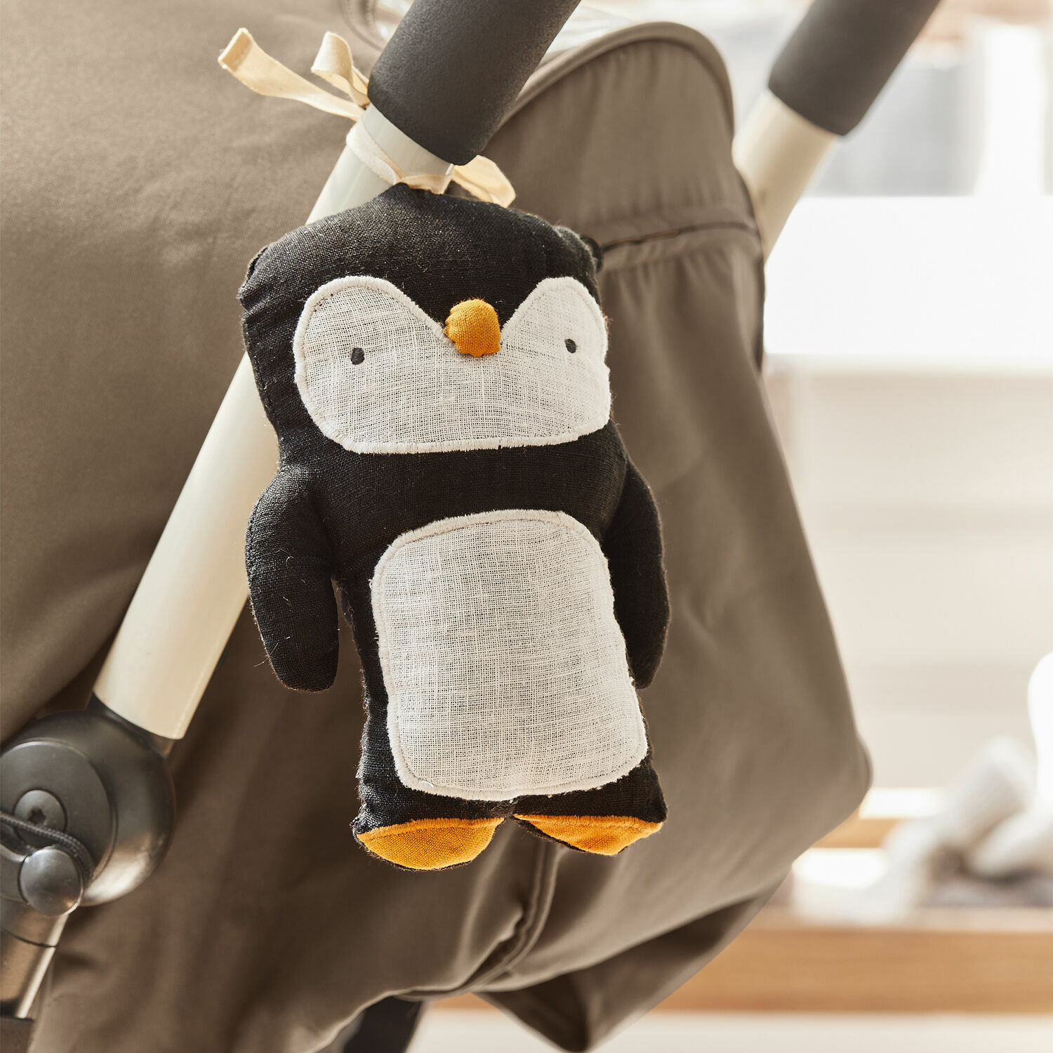 Kinderwagenanhänger Jocienne Schwarzer Plüsch-Pinguin mit weißem Bauch und orangen Füßen an Kinderwagen befestigt
