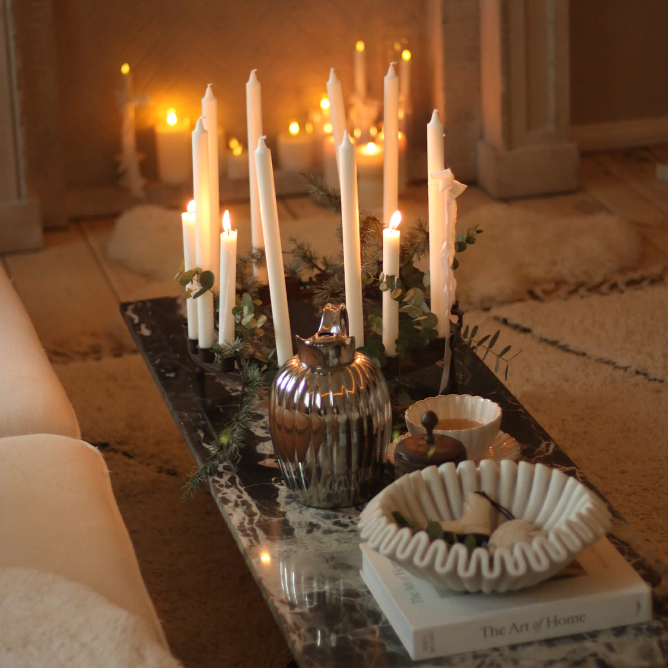 Dekorativer Kerzenhalter mit weißen Kerzen auf Marmorplatte mit Keramikschale und Metallkanne