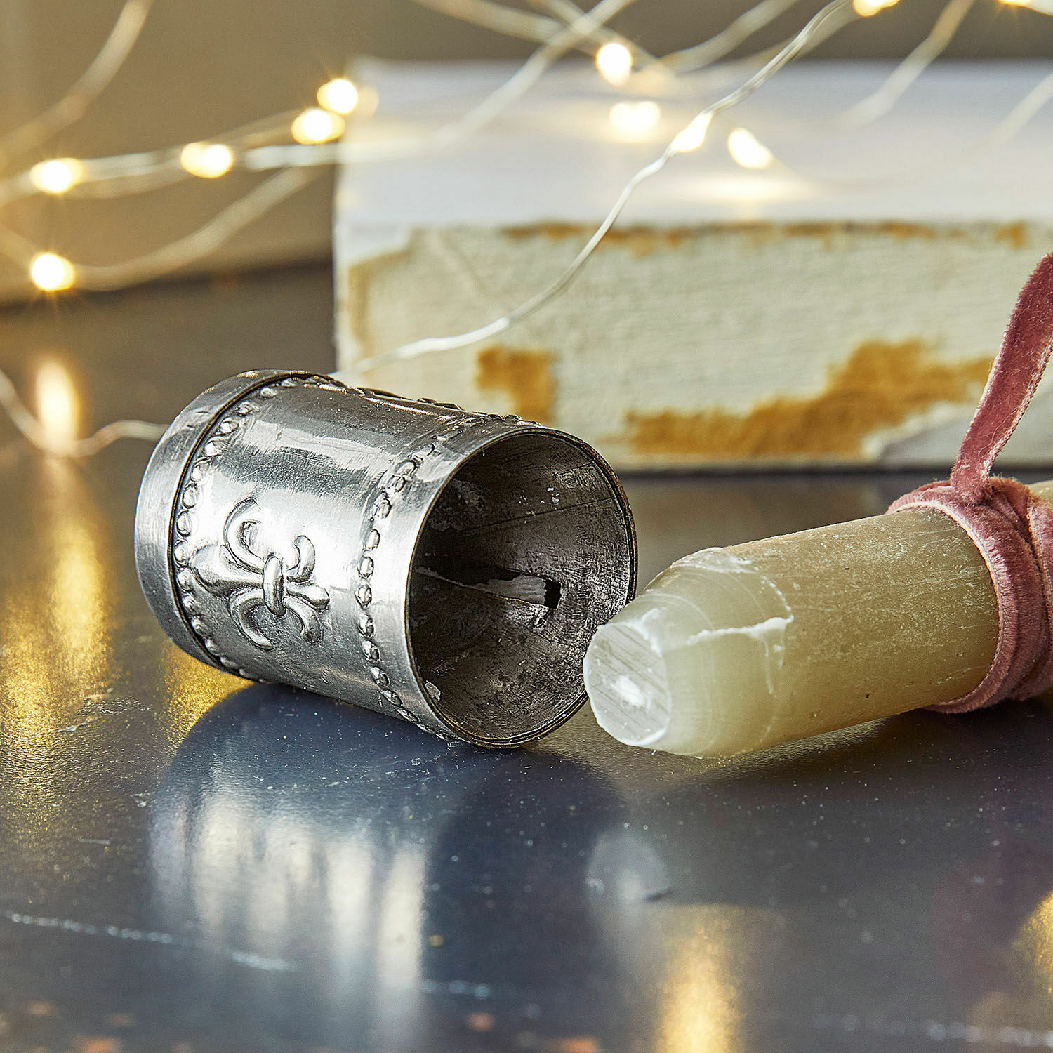 Kerzenanspitzer Fleur De Lys Silberner Metall-Napf mit dekorativem Muster auf Tisch mit Stein und Lichterkette