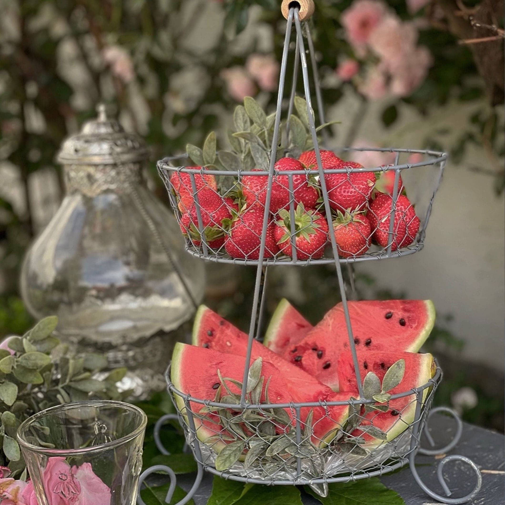 Zweistöckiger Metallkorb mit Erdbeeren und Wassermelonenstücken für sommerlichen Gartentisch
