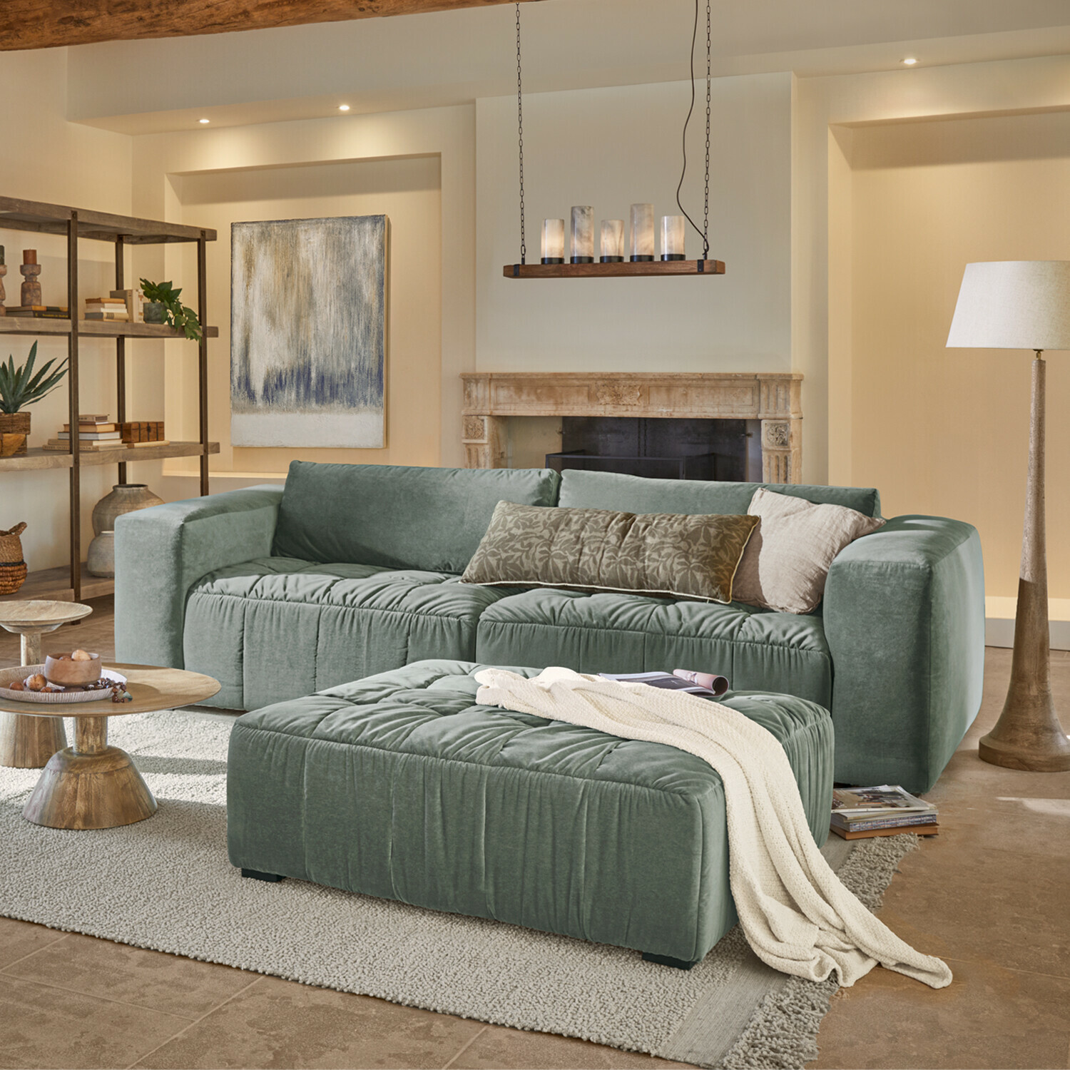 Sofa Ottolline Grünes Samtsofa mit Kissen und Hocker in gemütlichem Wohnzimmer mit Kamin und Stehlampe