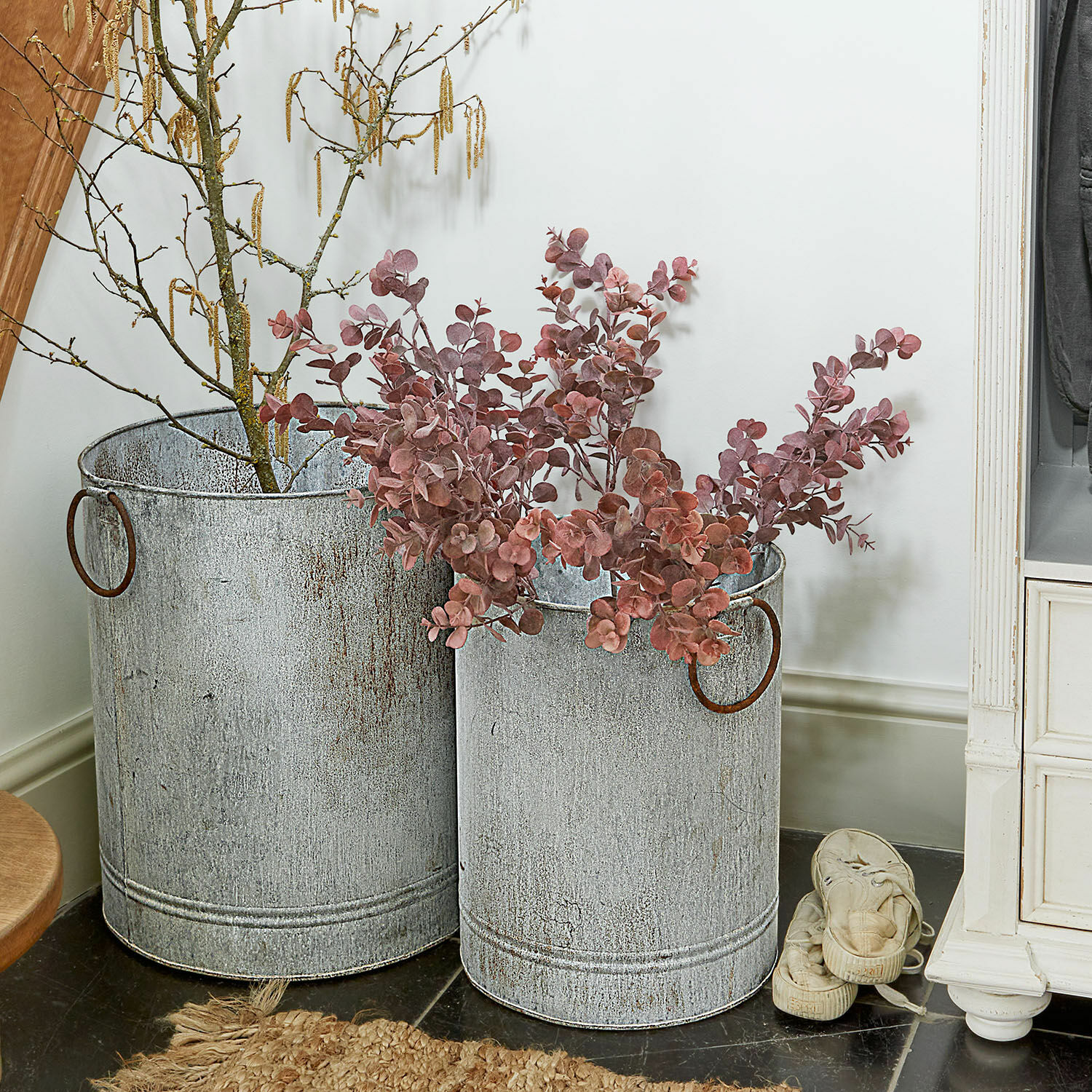 Zwei graue, antik wirkende Metallbehälter mit Griffen, dekoriert mit Zweigen und roten Blättern