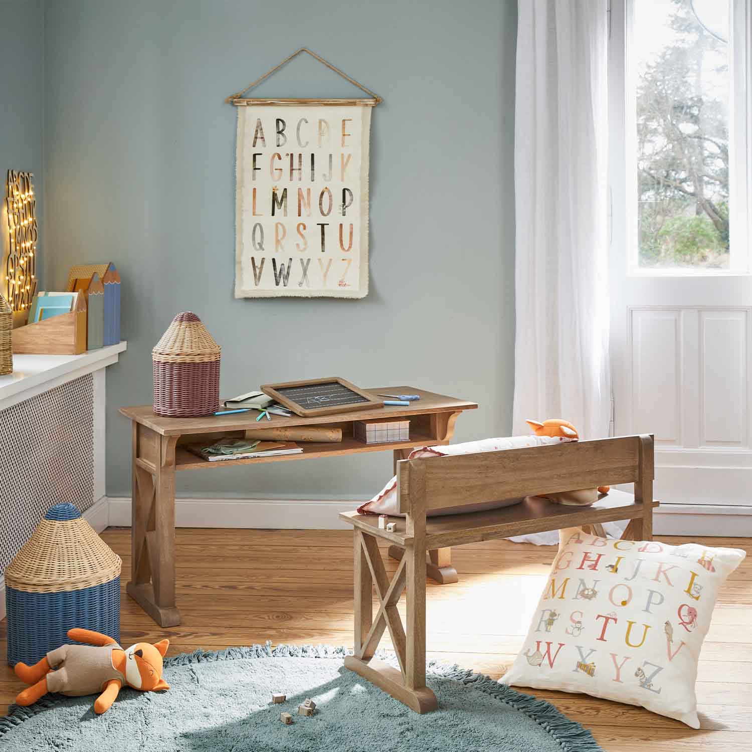 Kinderzimmer mit Holzschreibtisch und Bank, Kissen und Alphabet-Wandbehang in Pastellfarben