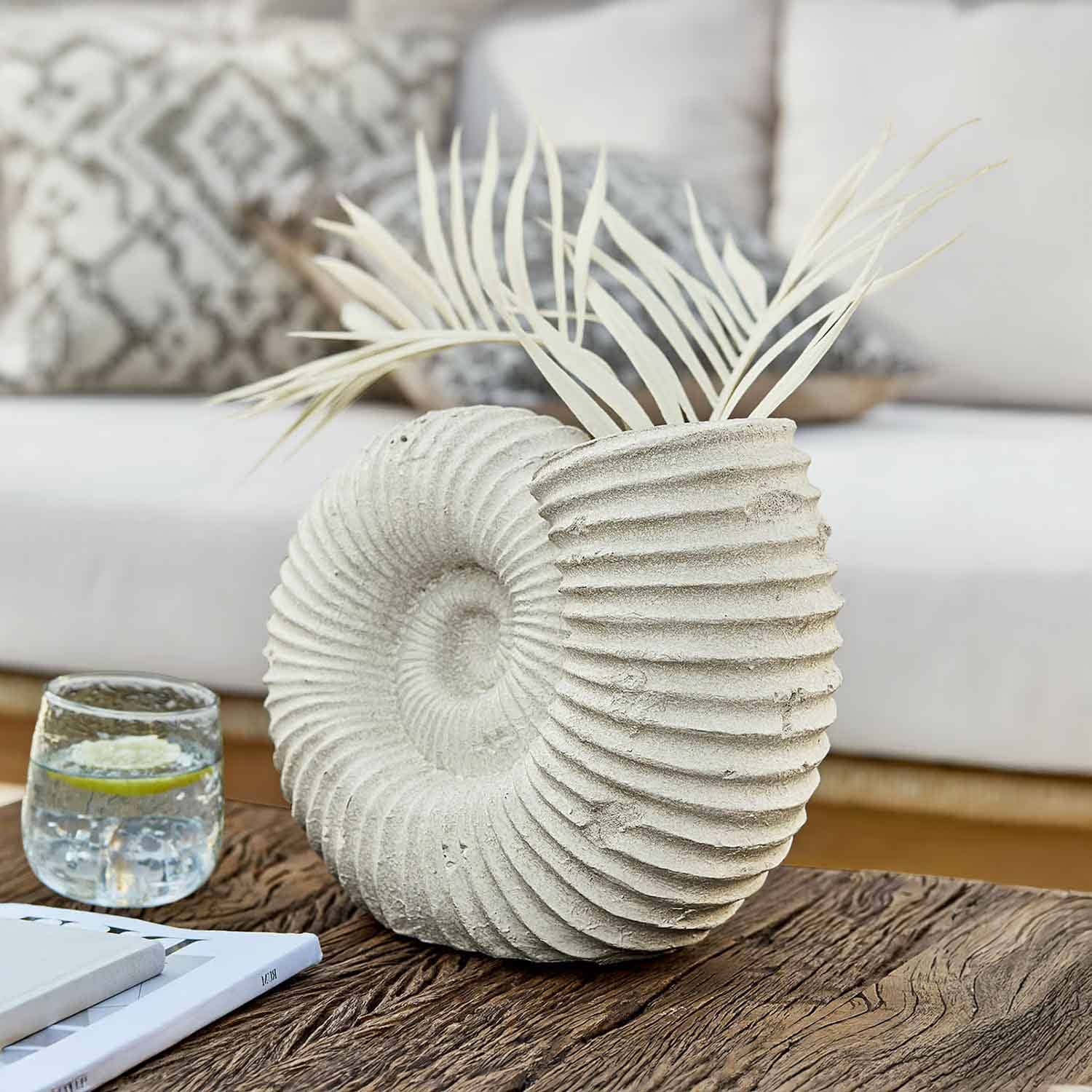 Dekorativer hellsteinfarbener Muschel-Vase mit getrockneten Blättern auf Holztisch