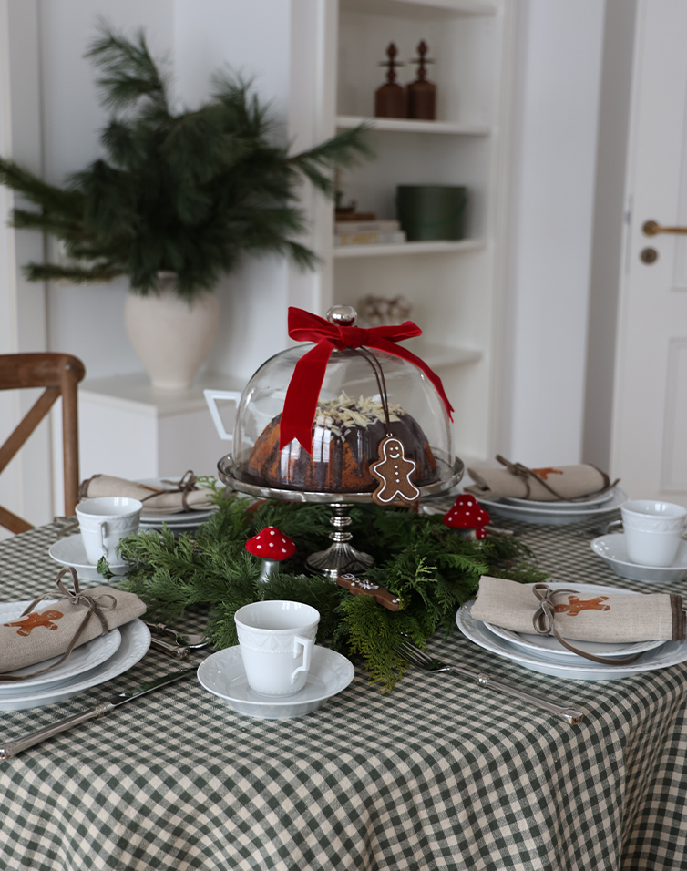 Festlich gedeckter Tisch mit Kuchen unter Glashaube, grünen Zweigen und roten Pilzdekorationen