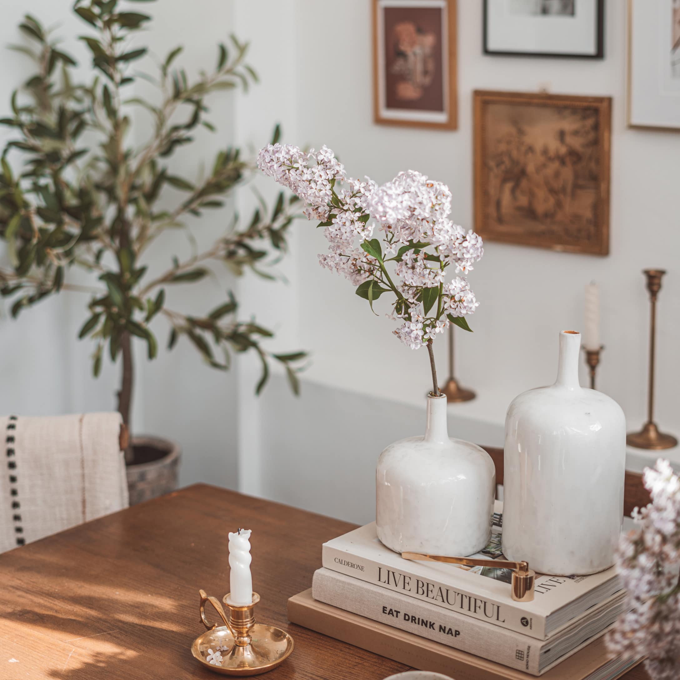 Weiße Keramikvasen mit Blumen auf Holztisch neben dekorativen Büchern in gemütlichem Wohnraum