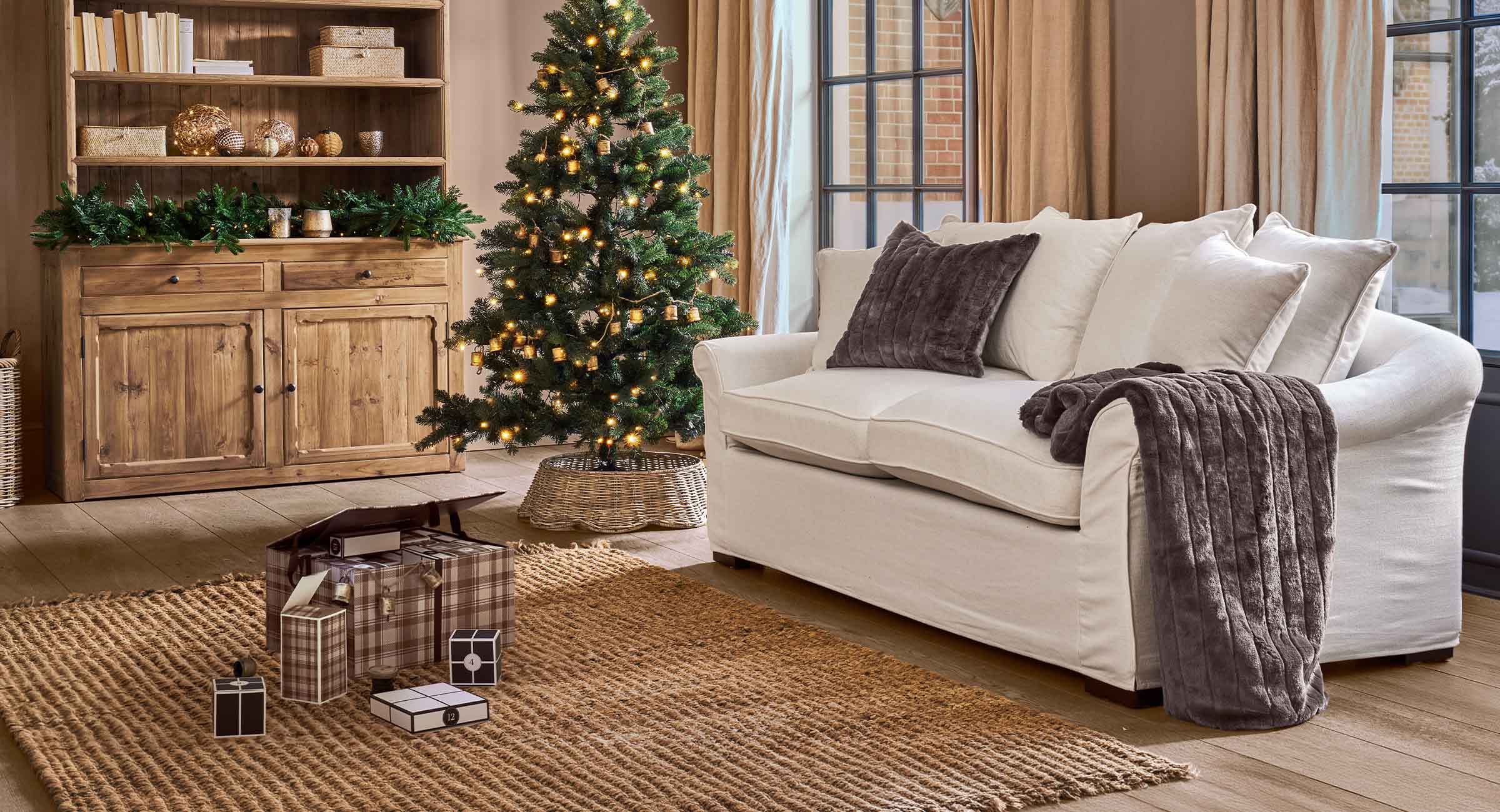 Gemütliches Wohnzimmer mit weißem Sofa, braunen Kissen und beleuchtetem Weihnachtsbaum