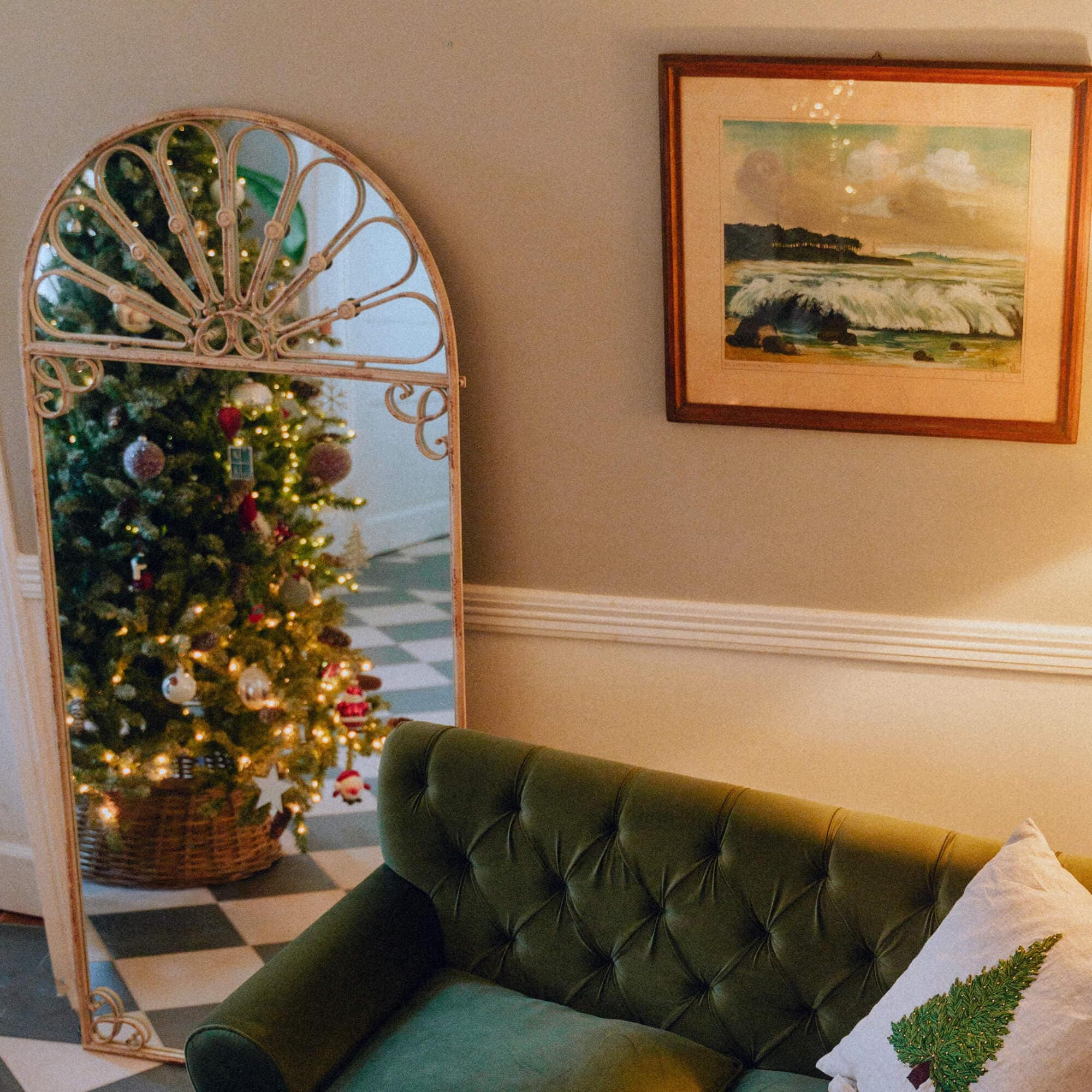 Dekorativer Spiegel mit Metallrahmen, der einen Weihnachtsbaum in einem gemütlichen Wohnzimmer mit grünem Sofa reflektiert