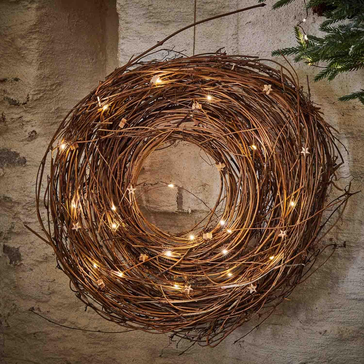 Dekorativer Kranz aus Naturzweigen mit zarten LED-Lichtern an der Wand