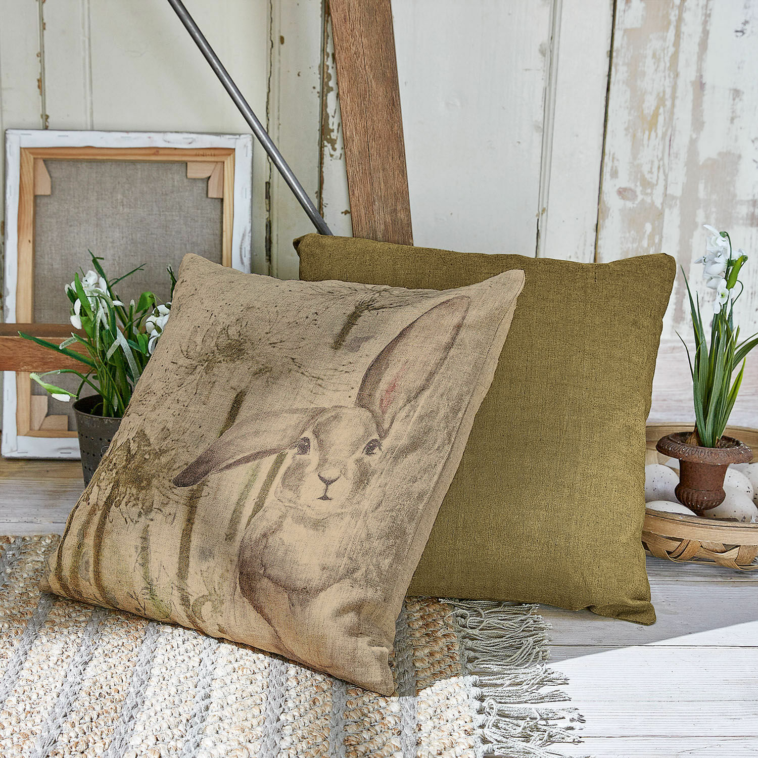 Kissenhülle 2er Set Milda Beige Kissen mit Hasenmotiv und grünes Dekokissen auf gewebtem Teppich