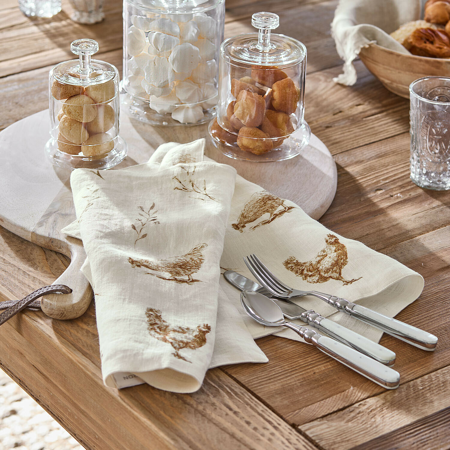 Leinenservietten in Creme mit braunem Hühnerdruck auf Holztisch mit Besteck aus Metall