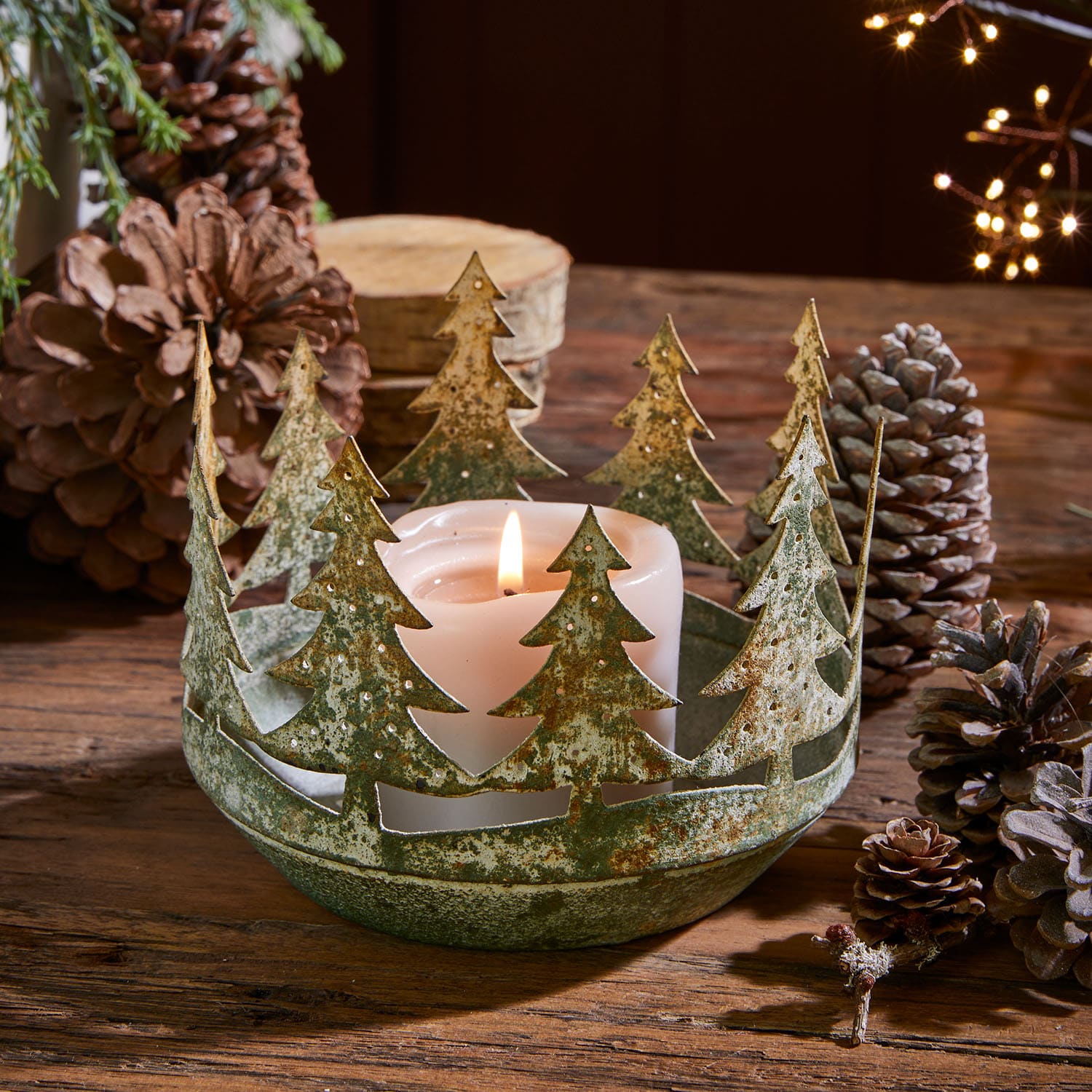 Metall-Kerzenhalter mit Tannenbaum-Motiv in grün-roster Optik und weißer Kerze auf Holztisch