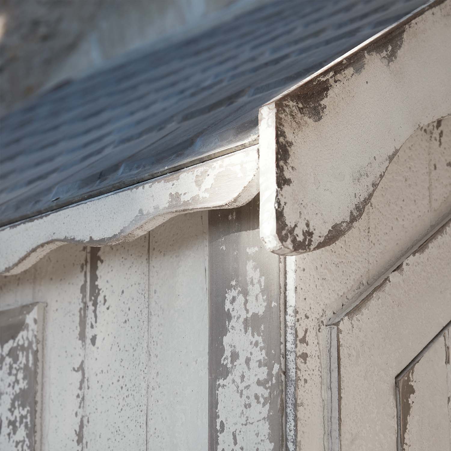 Nahaufnahme einer verwitterten weißen Holzkonstruktion mit Metalldach und geschwungener Kante