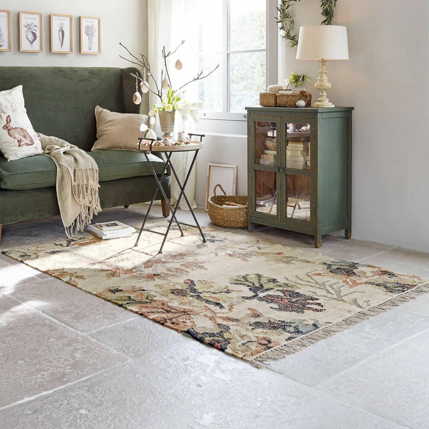 Gemütliches Wohnzimmer mit grünem Sofa, Holzschrank und floralem Teppich auf hellem Boden