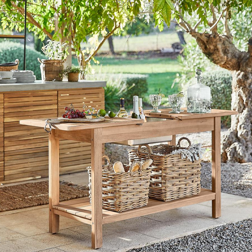 Gartentisch aus Naturholz mit geflochtenen Körben und Servierutensilien auf sonniger Terrasse