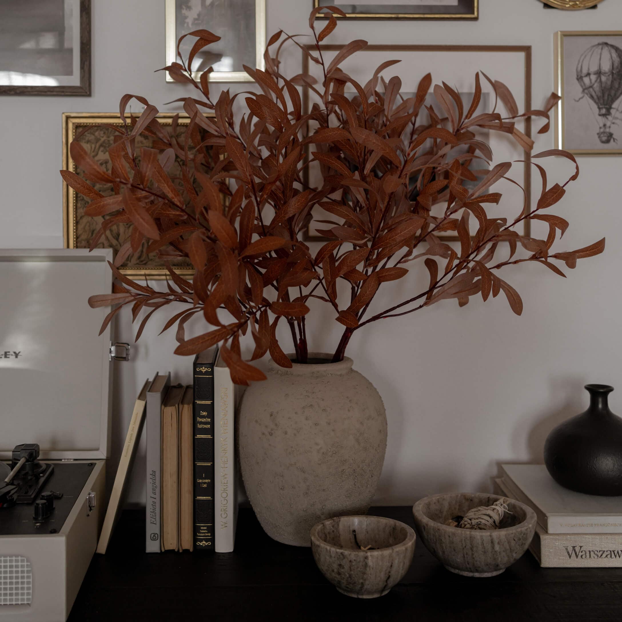 Beiger Alabastervase mit getrockneten braunen Zweigen auf dunklem Tisch mit Büchern und Dekoration