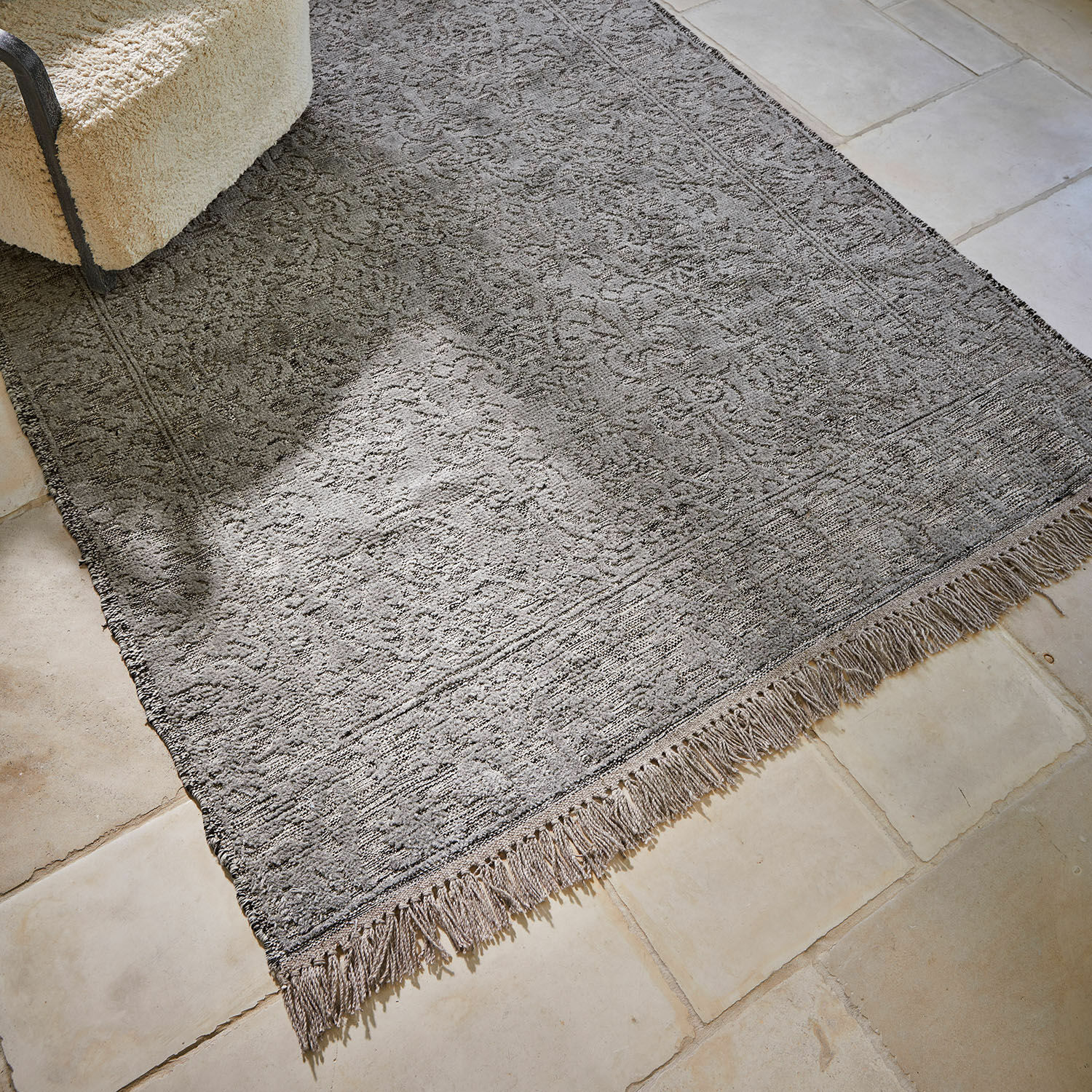 Grauer Teppich mit Fransen und feinem Muster auf hellem Boden, stilvolle Raumdekoration