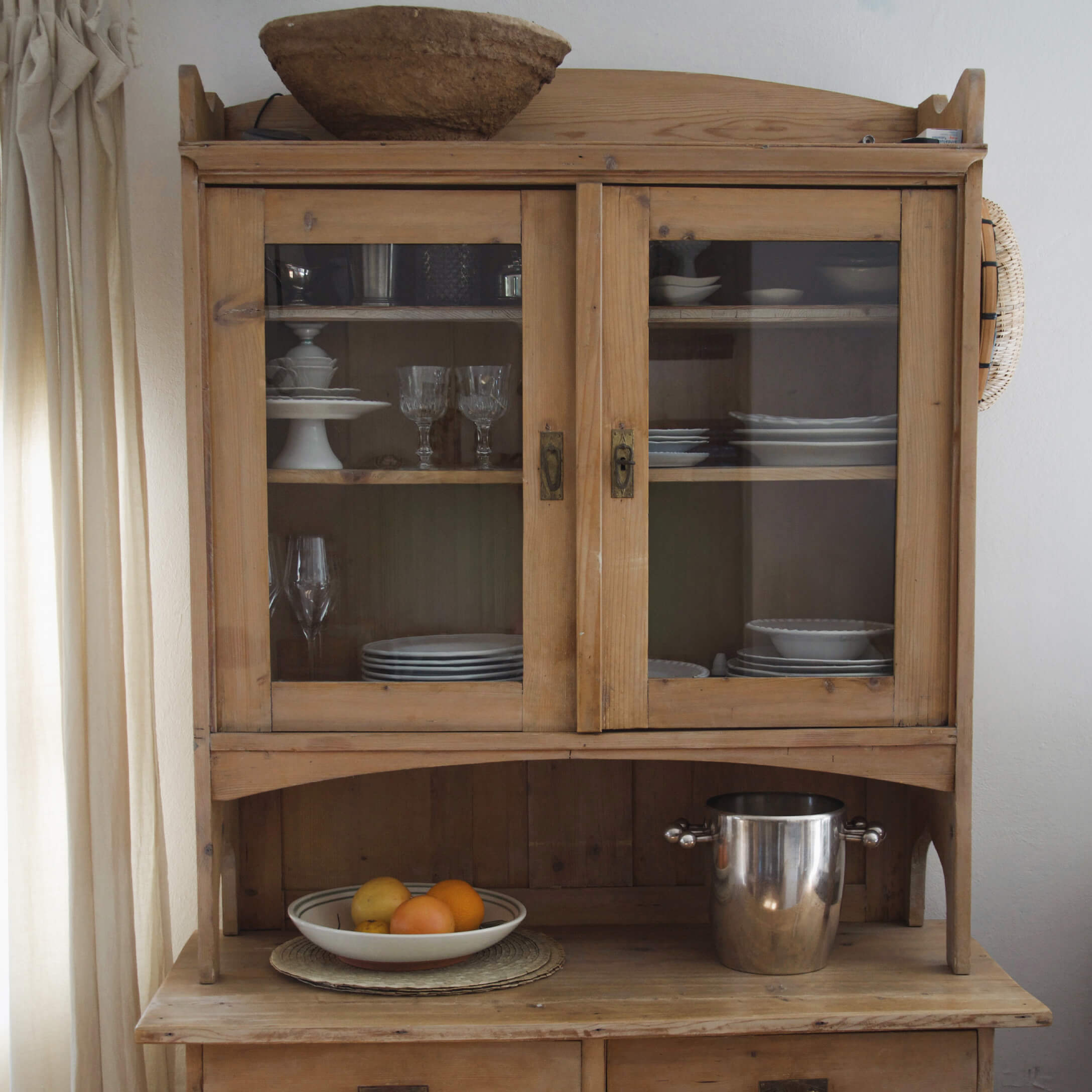 Holz-Küchenschrank mit Glastüren, weißem Geschirr und Metall-Eiskübel auf der Ablage