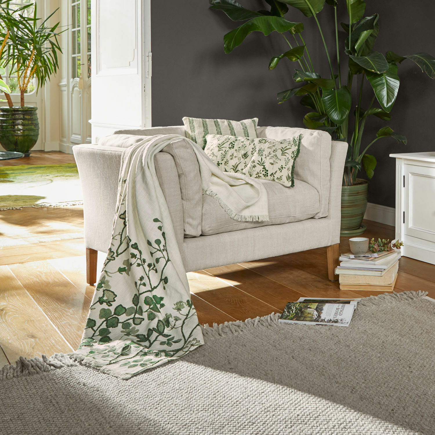 Sessel Lourvière Beiges Stoffsofa mit grünen Kissen und dekorativer Decke mit Pflanzenmuster im Wohnzimmer
