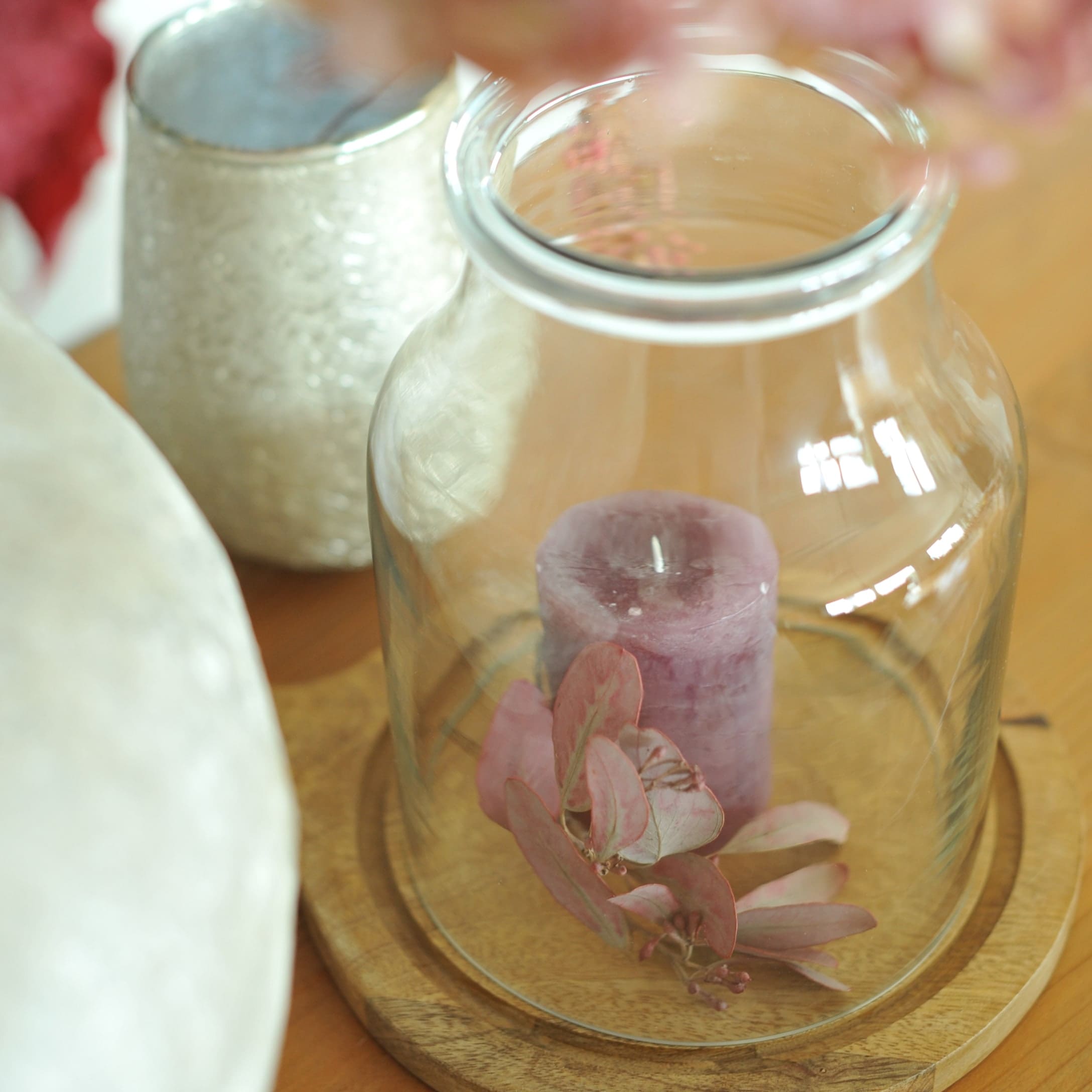 Glasvase aus klarem Glas auf Holzunterlage mit lila Kerze und getrockneten Blättern dekoriert