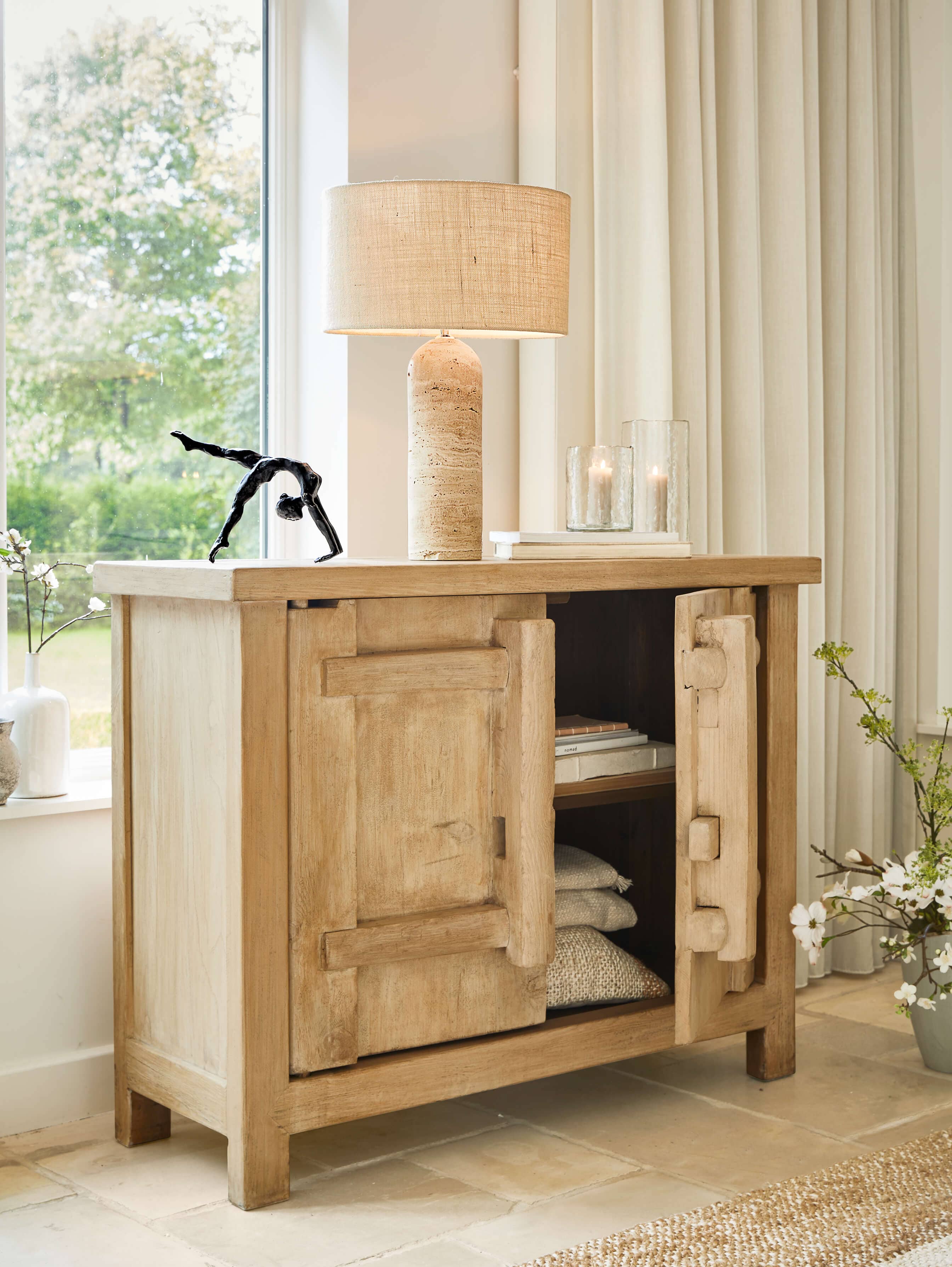 Helle Holzkommode mit offenen Türen, beiger Lampe und Dekoration in hellem Wohnzimmer