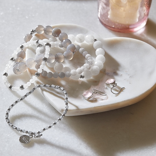 Schmuckset mit weißen und grauen Perlen sowie rosa Ohrringen auf Marmorplatte
