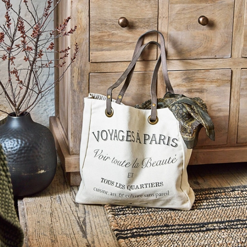 Beige Baumwolltasche mit schwarzem Schriftzug und braunen Griffen auf Holzboden