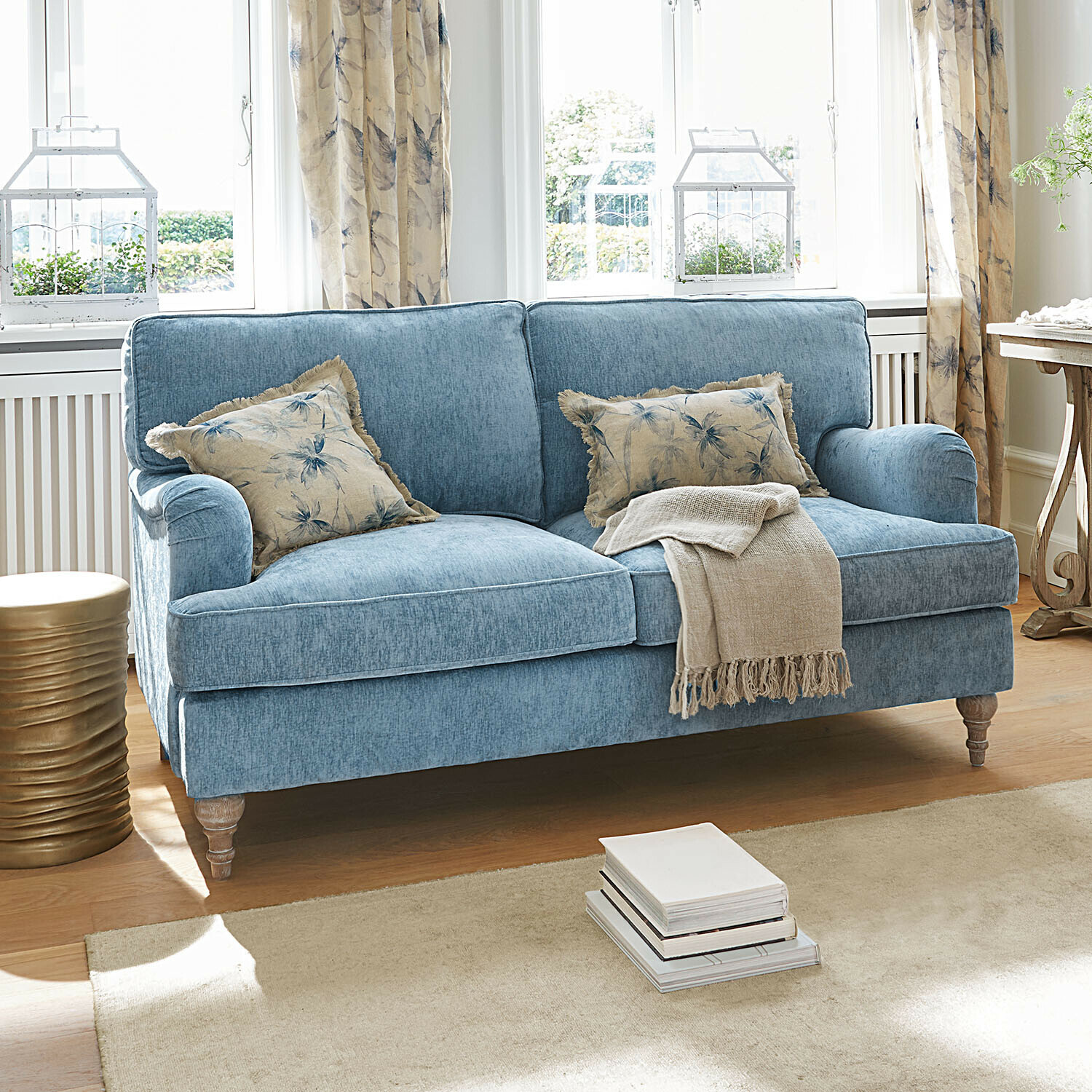 Blaues Stoffsofa mit floral gemusterten Kissen und beiger Decke in hellem Wohnzimmer