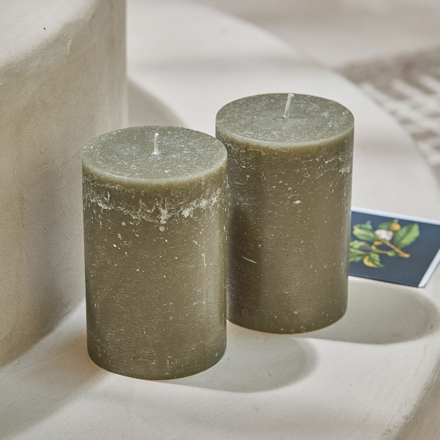 Zwei grüne Wachskerzen mit rustikaler Struktur auf hellem Untergrund als Wohnaccessoire