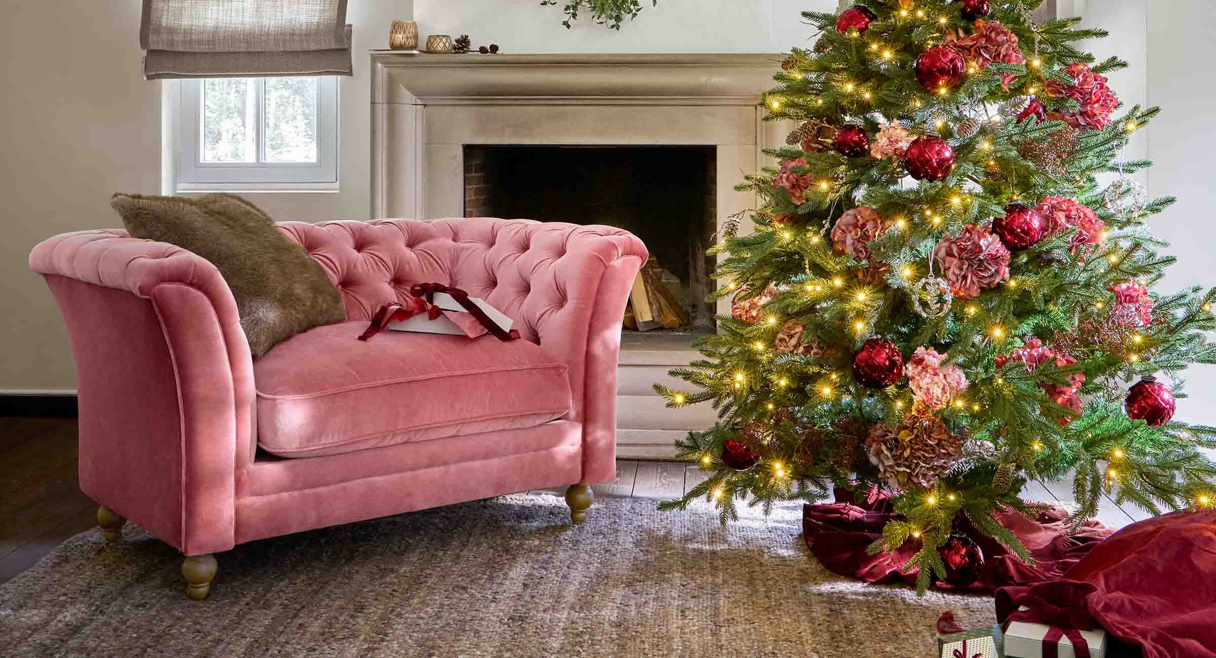 Rosa Samtsofa neben festlich geschmücktem Weihnachtsbaum mit roten Kugeln und Lichterketten