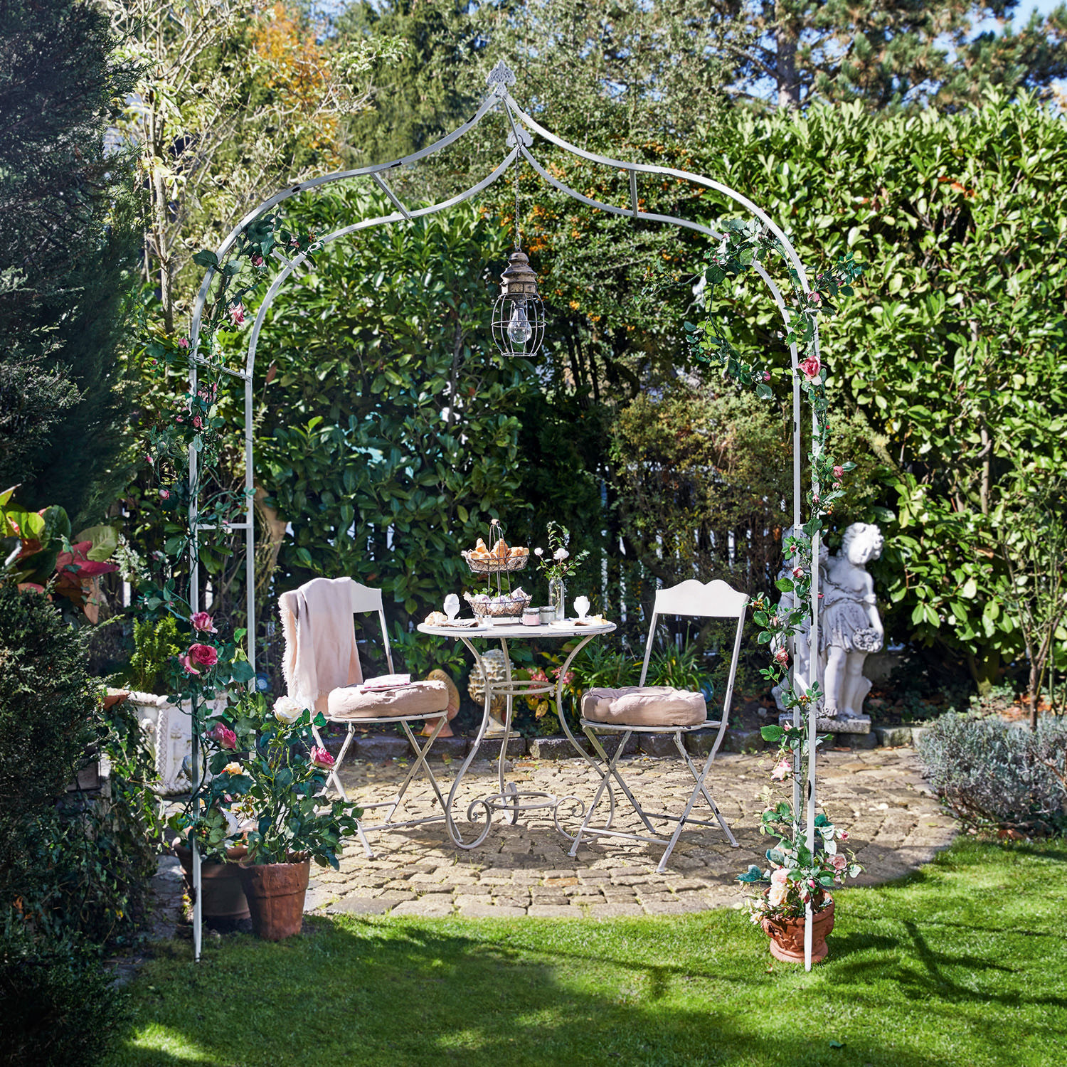 Rosenbogen Dimarus Weißer Metall-Gartenbogen mit rosa Blumen und Hängelampe, davor Sitzgruppe auf Steinpflaster