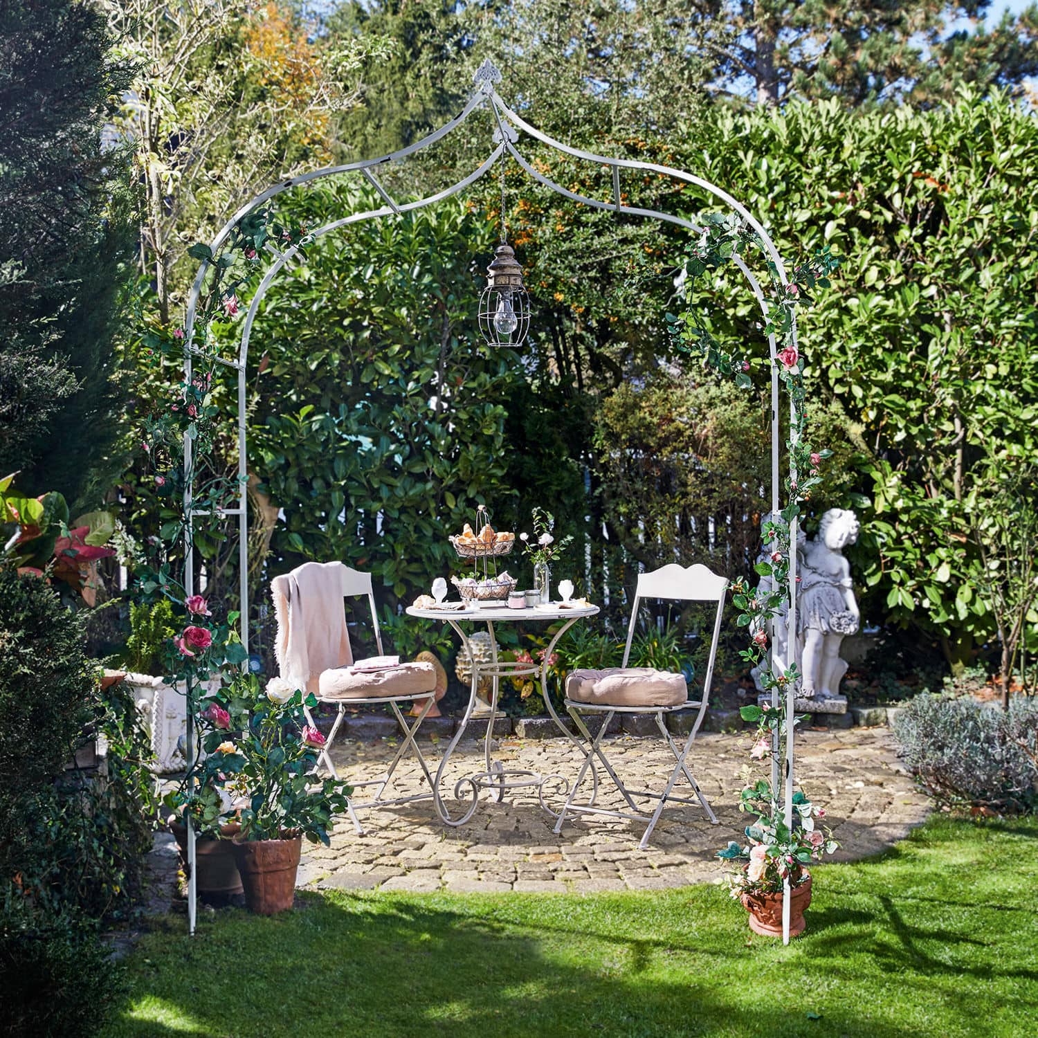 Rosenbogen Dimarus Weißer Metall-Gartenbogen mit rosa Blumen und Hängelampe, davor Sitzgruppe auf Steinpflaster