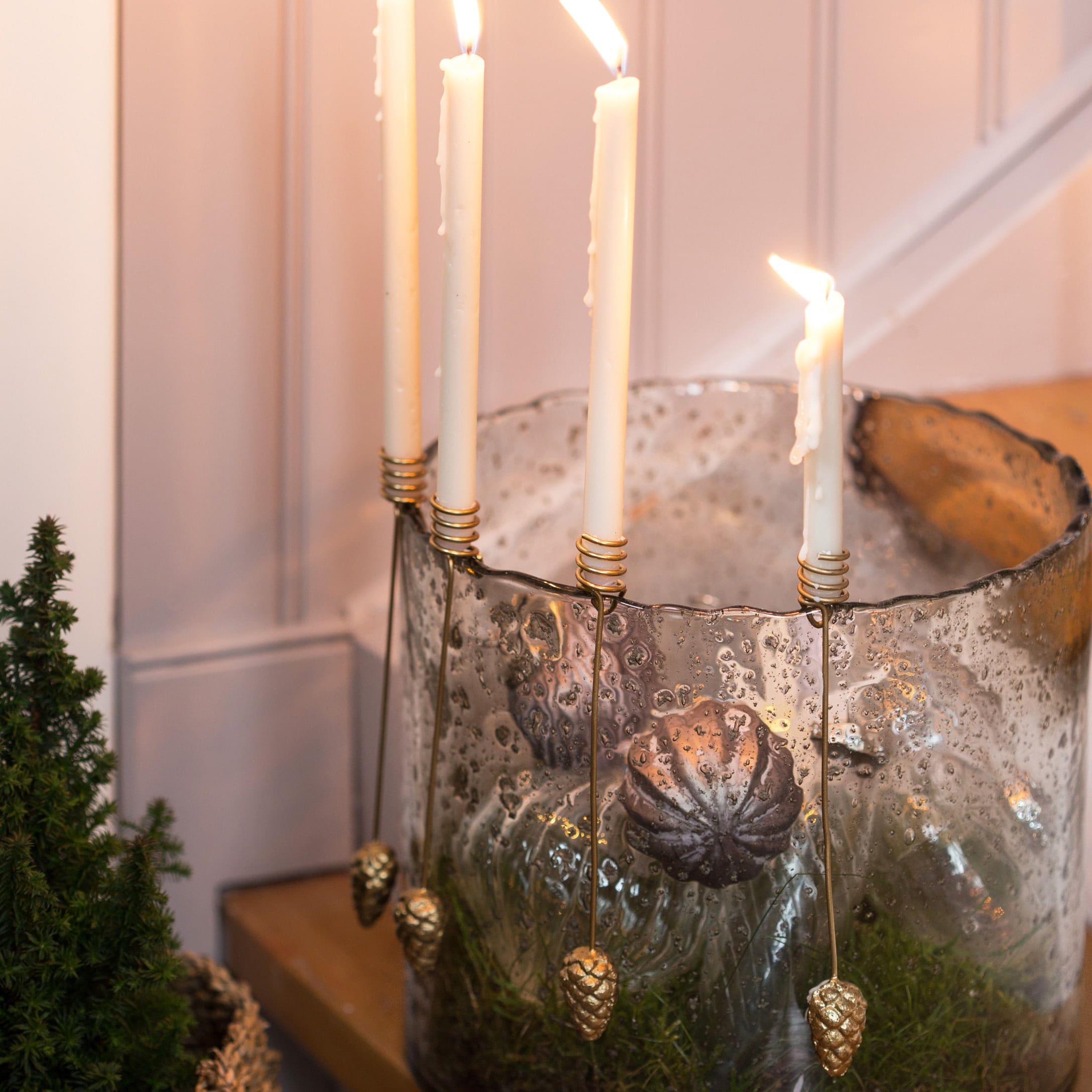 Glas-Kerzenhalter mit weißen Kerzen und goldenen Zapfenanhängern auf Holztisch dekoriert