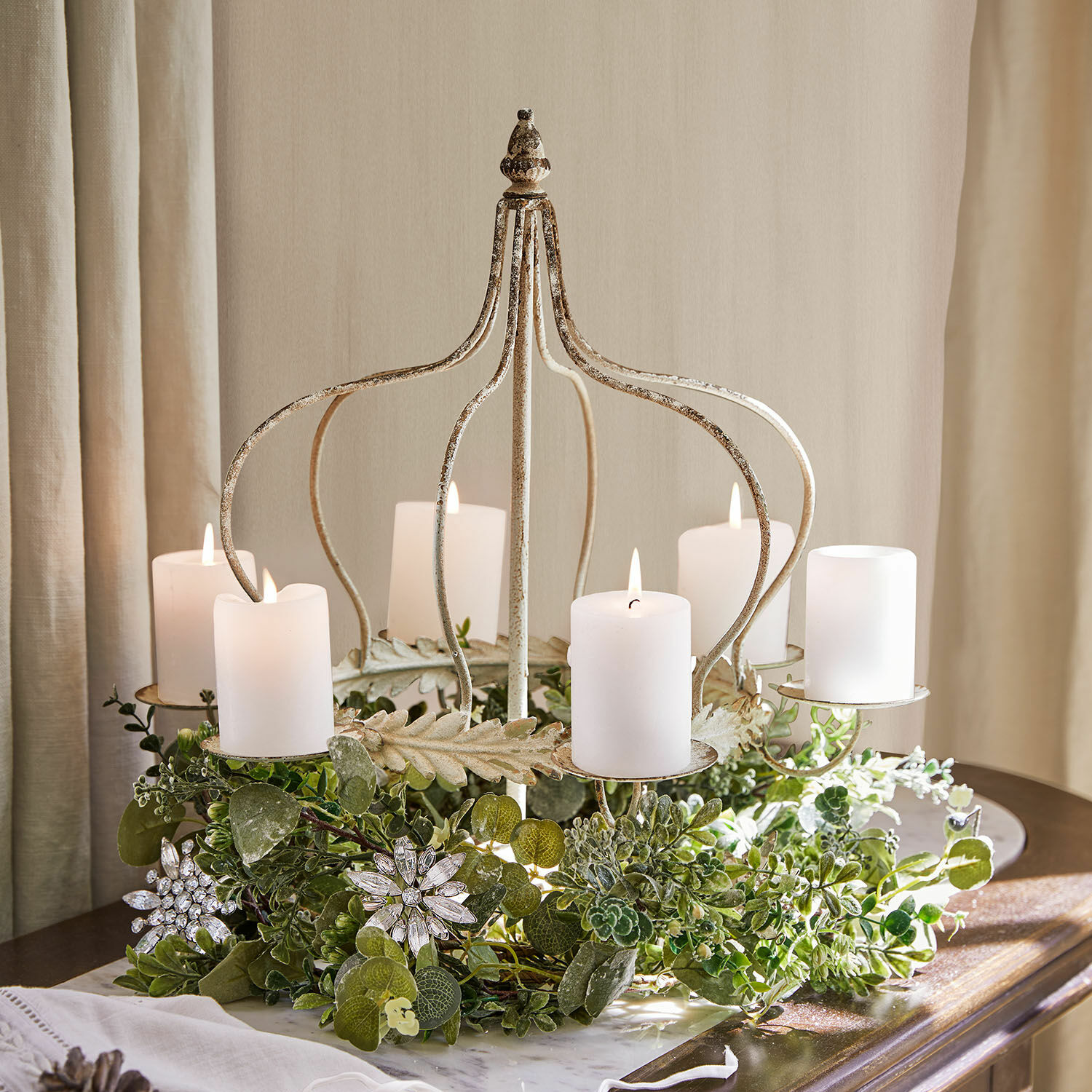 Metall-Kerzenhalter in Kronenform mit weißen Kerzen und grüner Dekoration auf Tisch