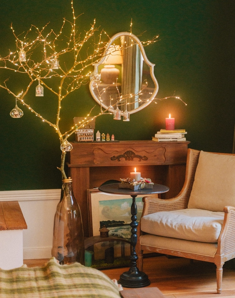Gemütliches Wohnzimmer mit grünem Wandton, beleuchtetem Deko-Baum und Kerzen auf Holzkommode