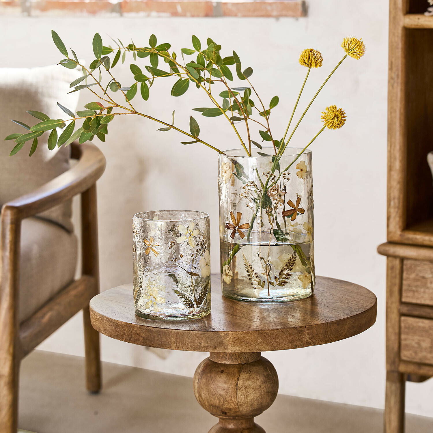 Glasvasen mit getrockneten Blumen und Blättern auf einem Holztisch in hellem Raum