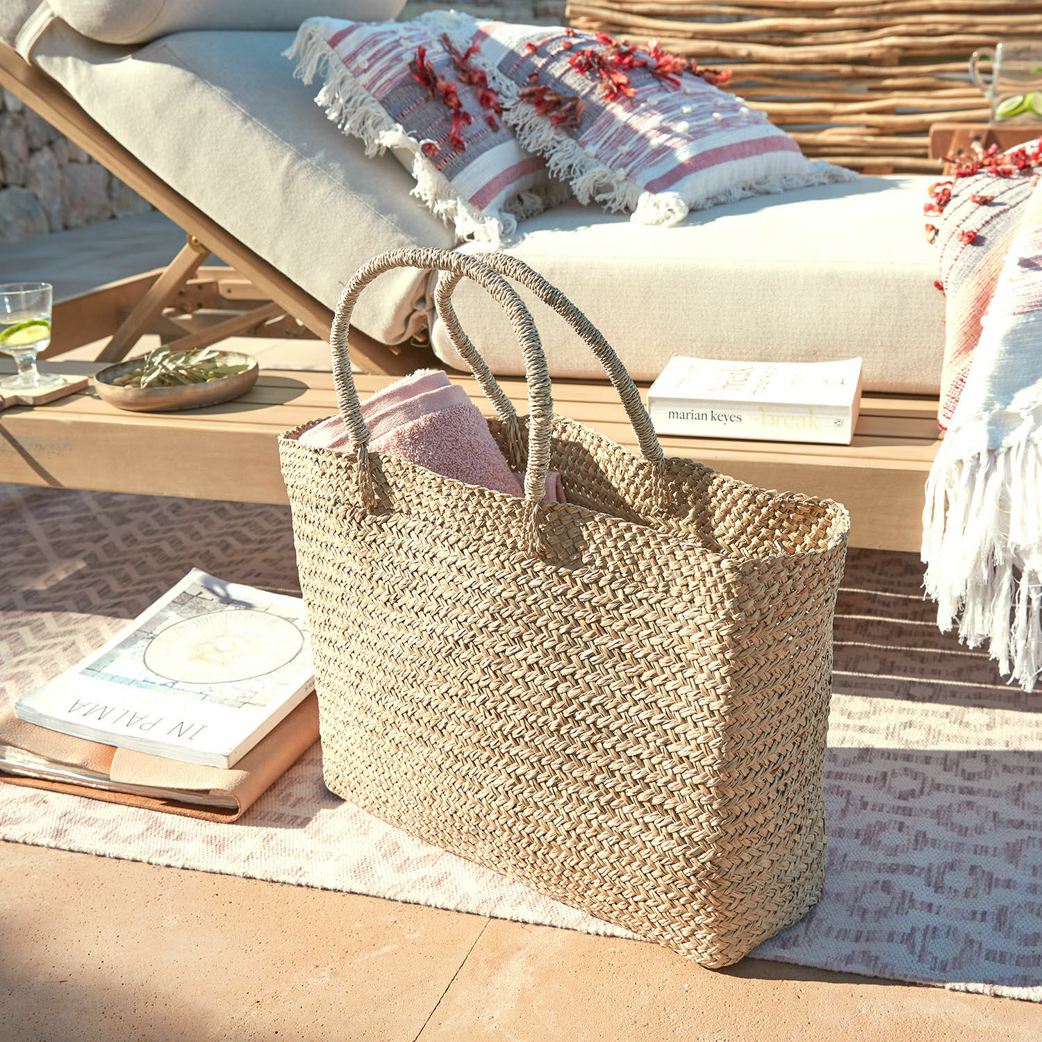 Tasche Ventresque Natürliche geflochtene Tasche aus Seegras mit rosa Handtuch auf Terrasse neben Liegestuhl