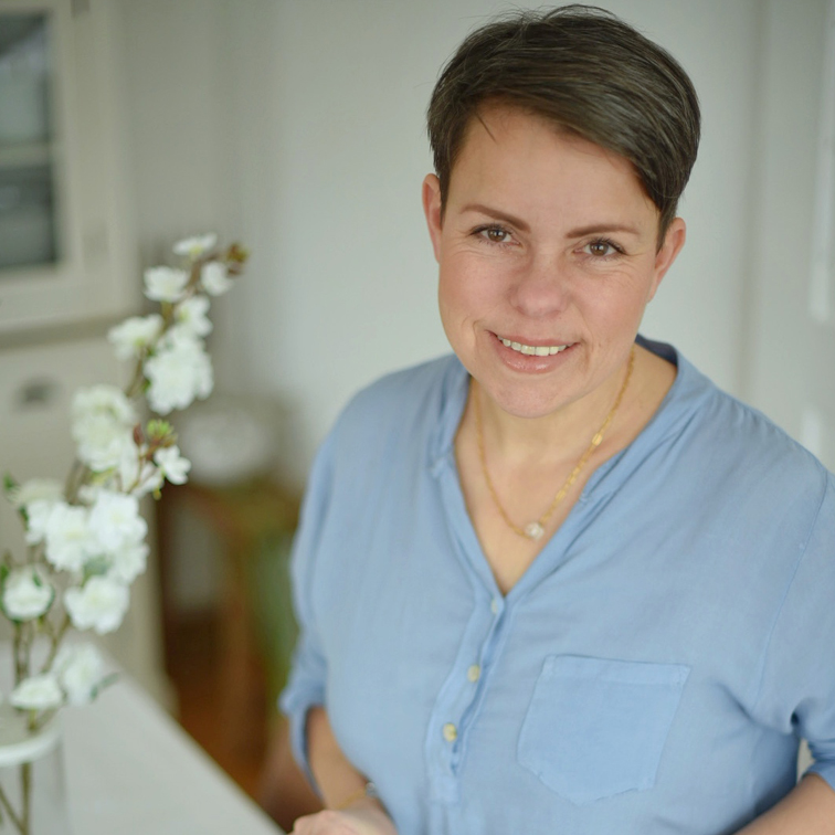 Lächende Frau in blauem Hemd neben weißen Blumen in hellem Raum