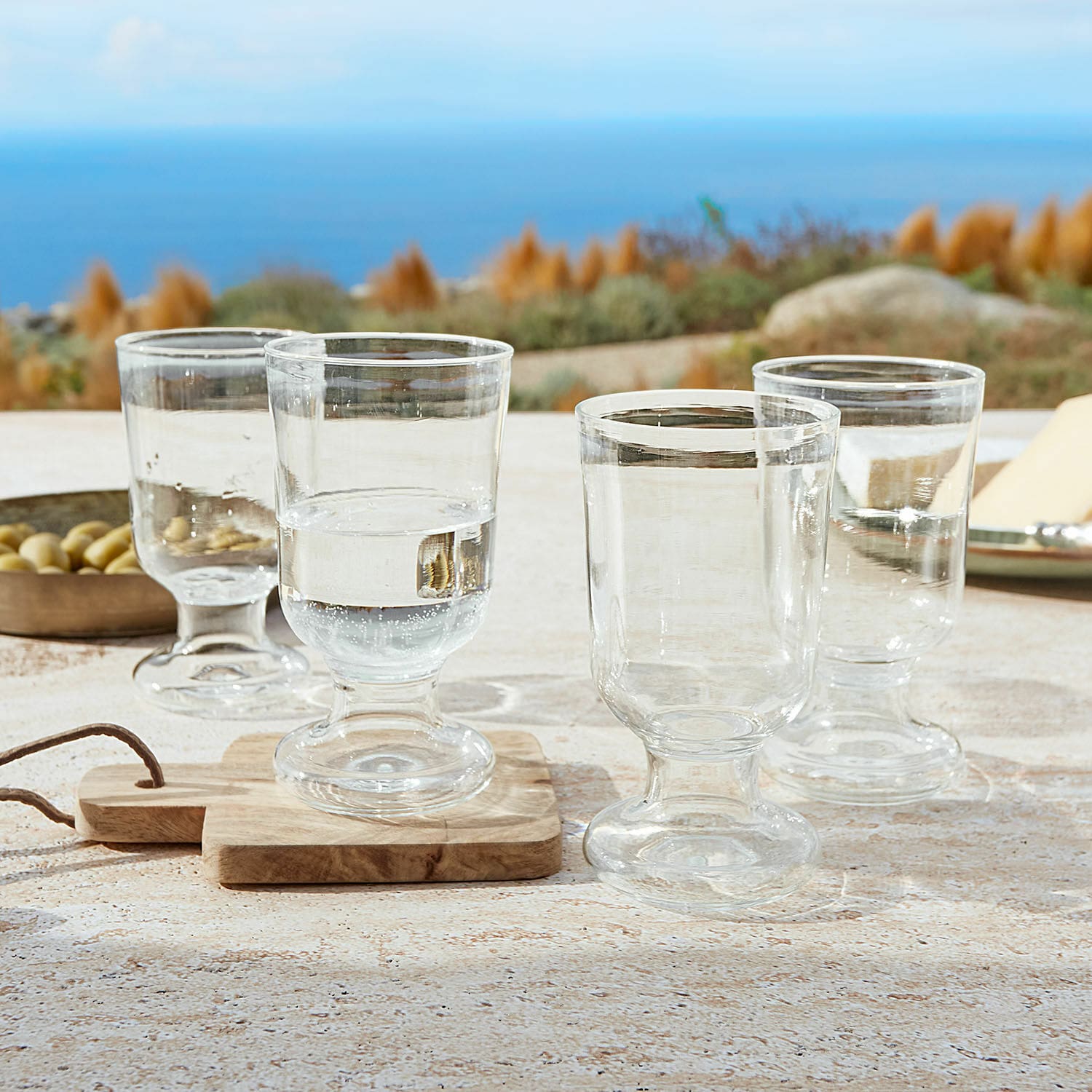 Glas 4er Set Yvoncourt Vier transparente Gläser auf Fuß auf Tisch mit Meerblick, modernes Trinkgeschirr