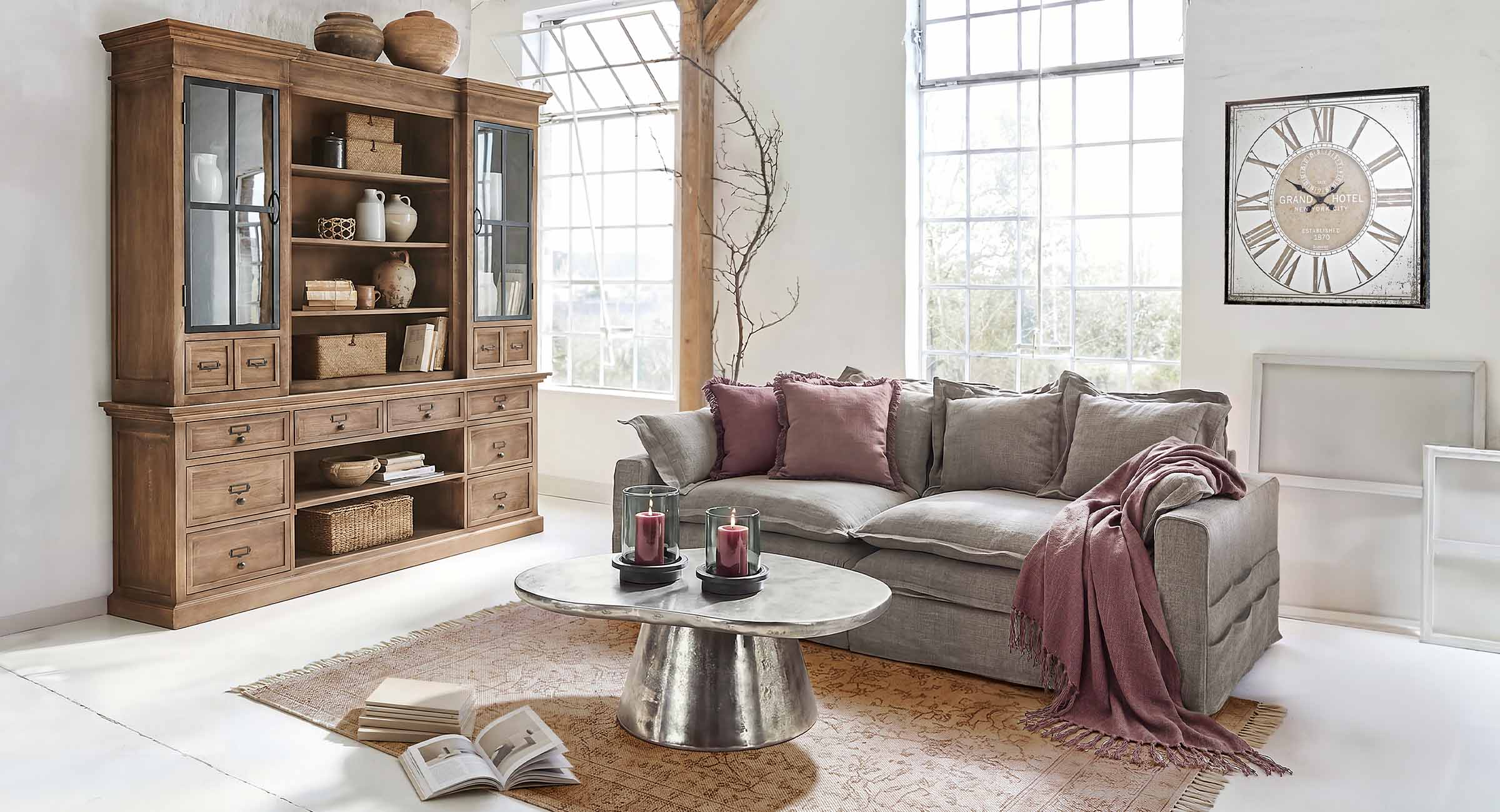 Gemütliches Wohnzimmer mit grauem Sofa, bordeauxfarbenen Kissen und antiker Holzwandvitrine
